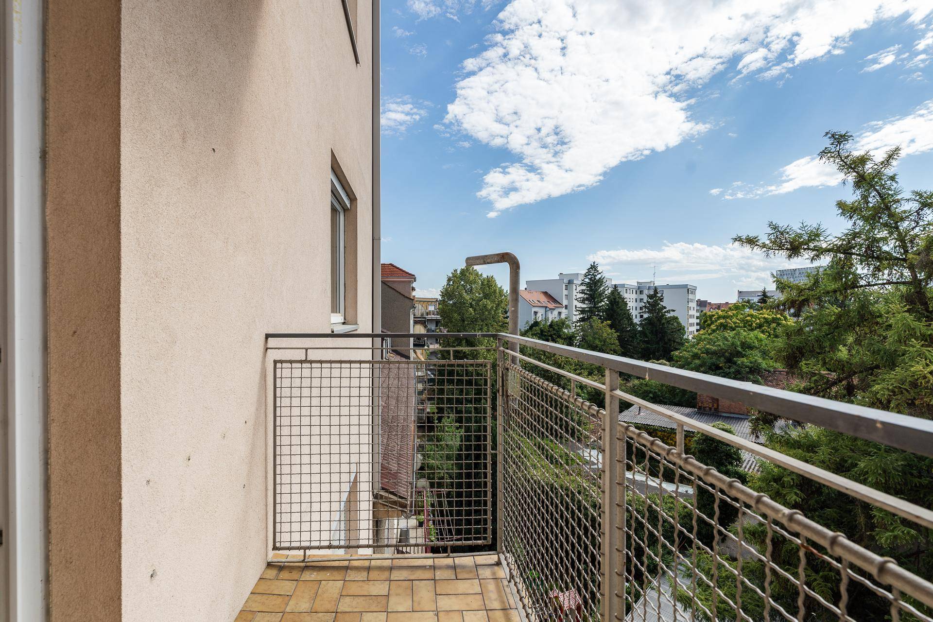 Kleiner Balkon mit Metallgeländer und Blick auf Bäume und umliegende Gebäude.