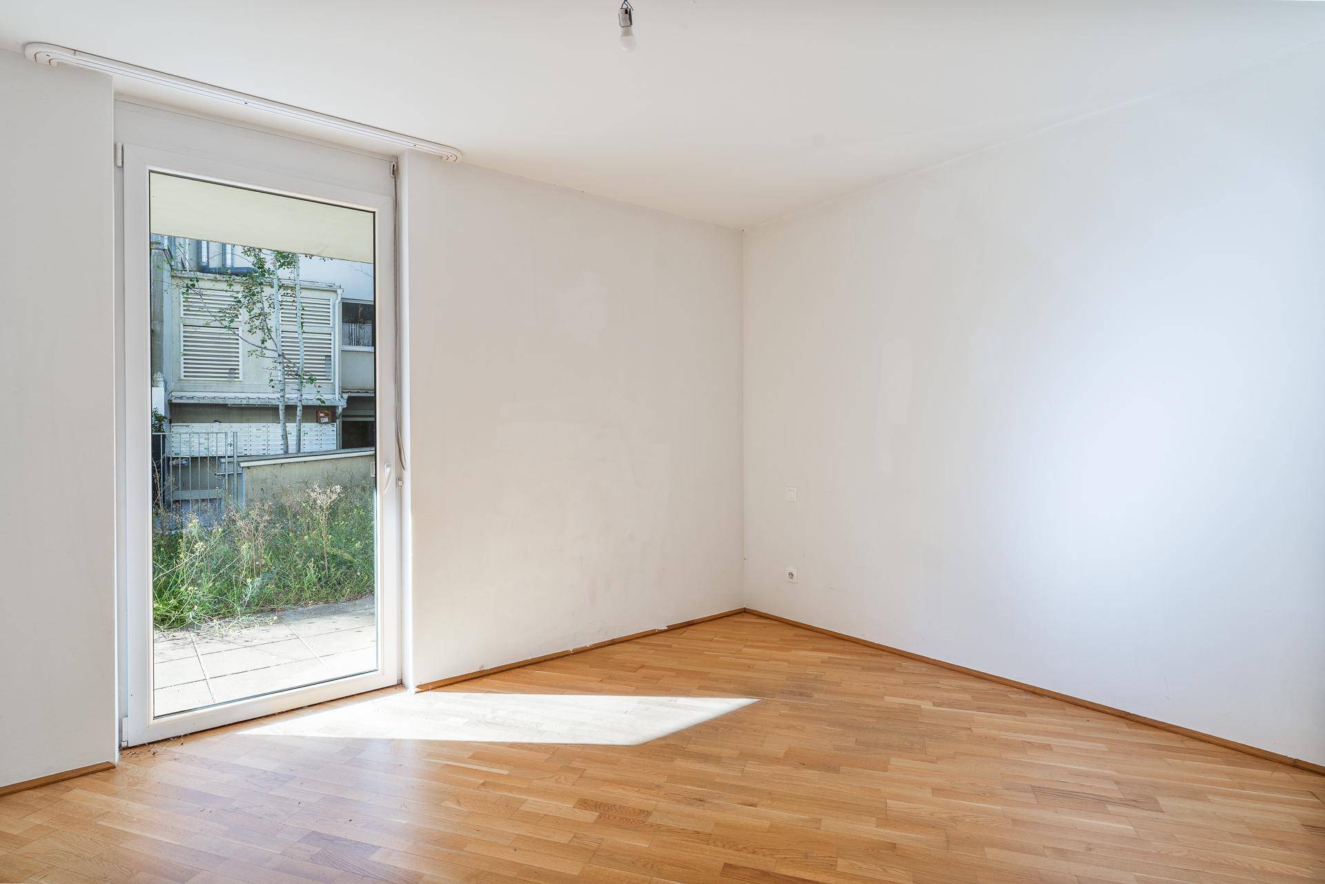 Lichtdurchfluteter Raum mit Holzboden und großer Glastür zum Außenbereich, ideal für Entspannung.