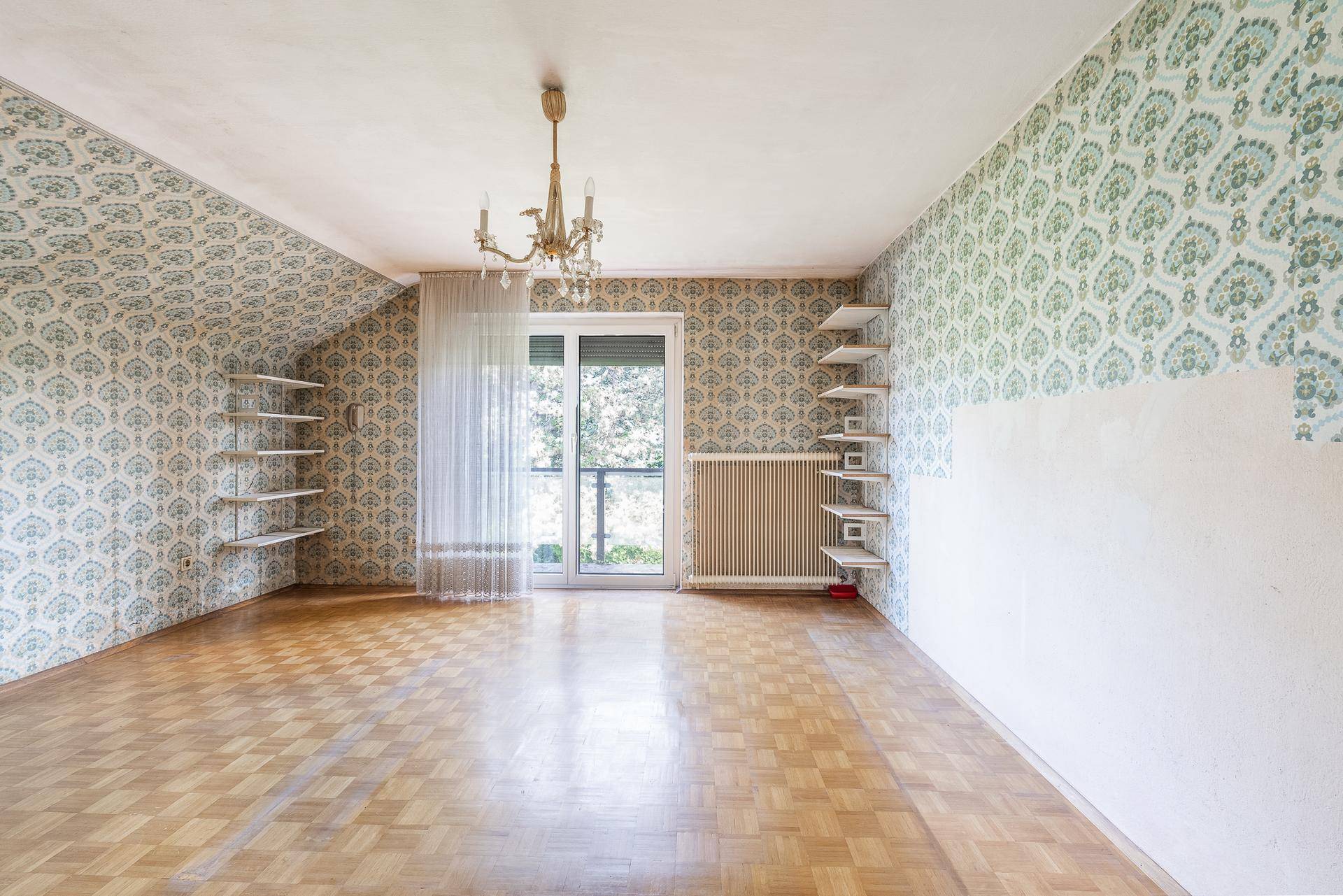 Helles Schlafzimmer mit gemusterter Tapete, Parkettboden und Balkonzugang.