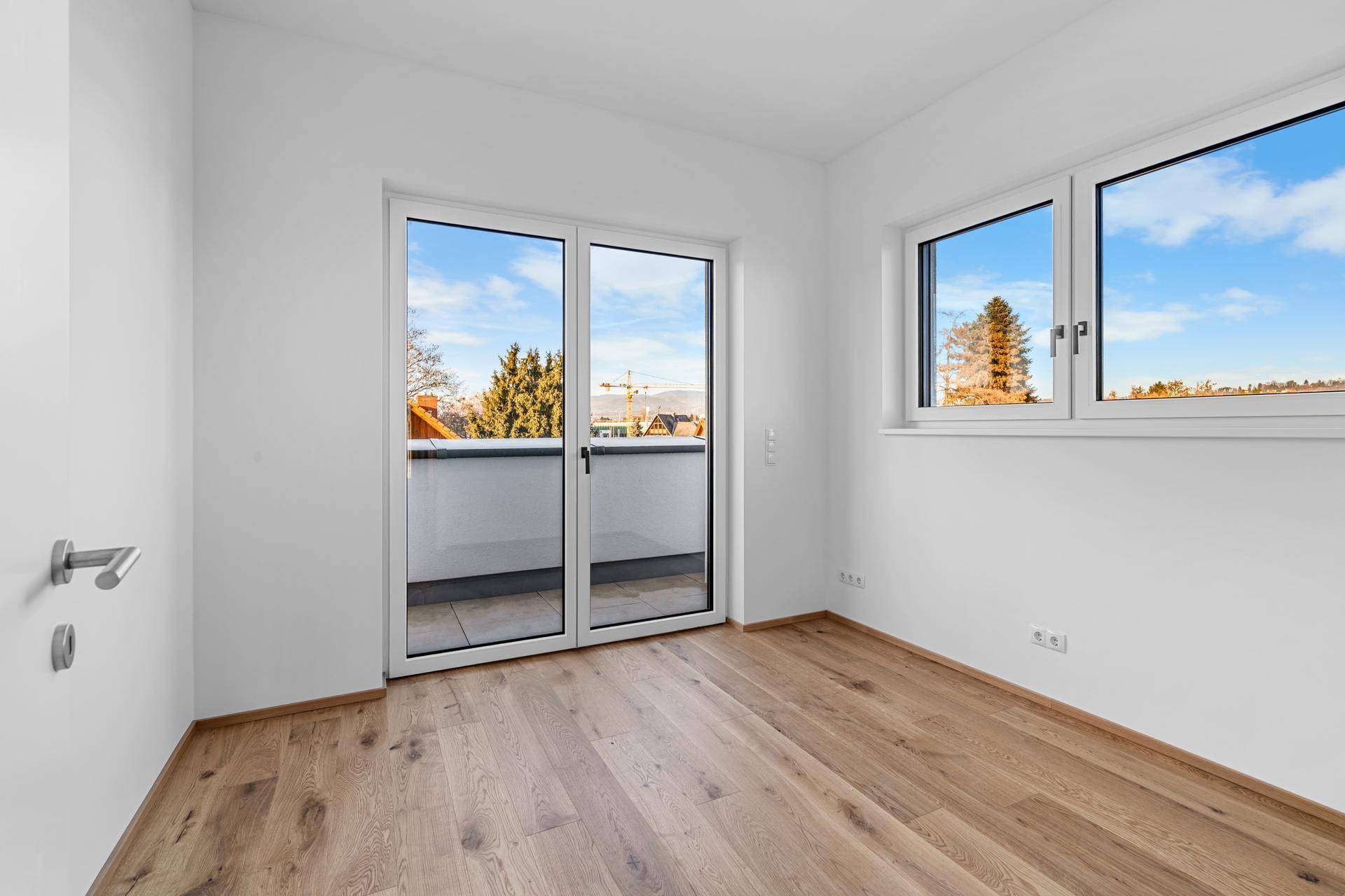 Helles Schlafzimmer mit Holzparkett und Fenstern, die einen Blick ins Grüne ermöglichen.