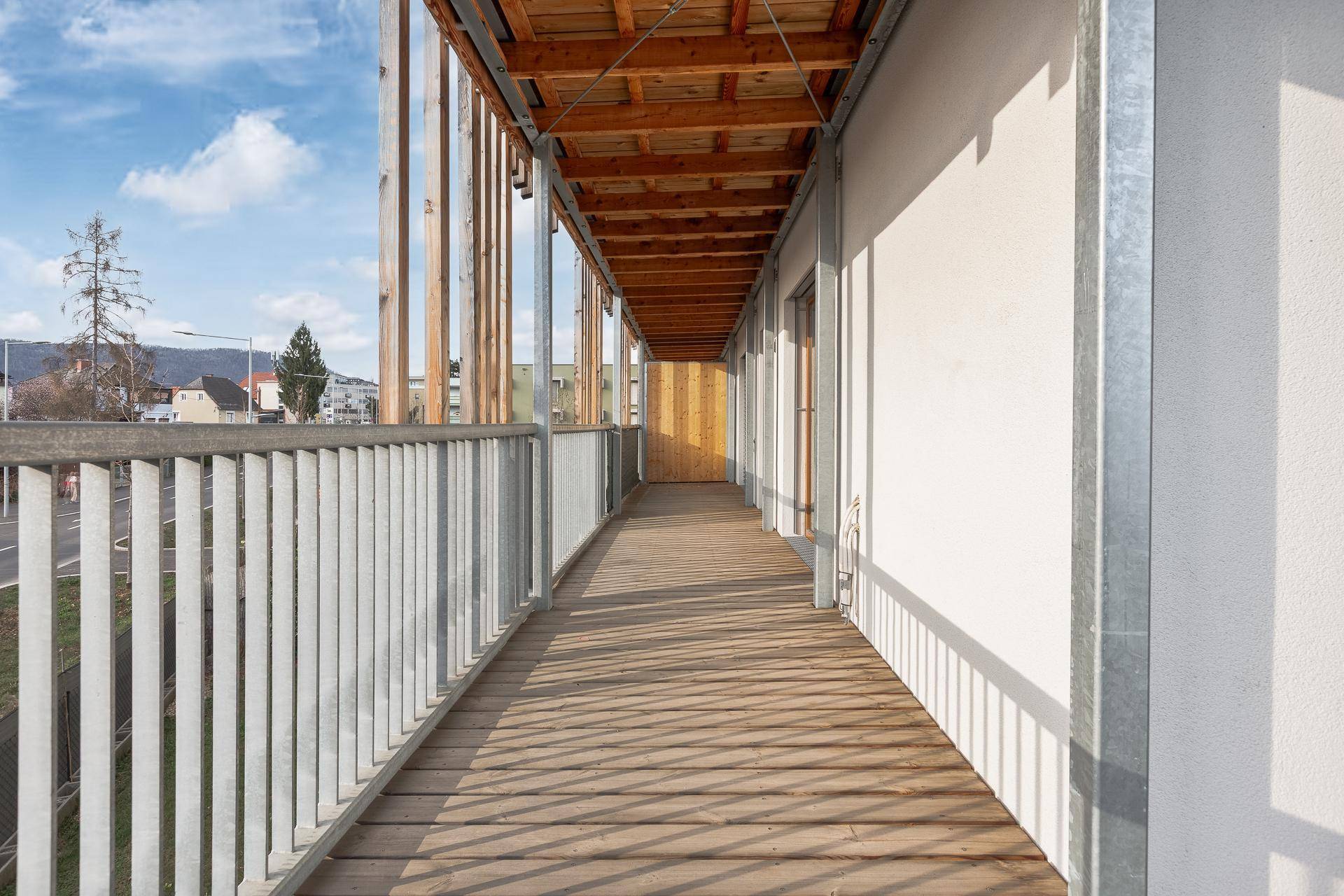 Langer überdachter Balkon mit Holzboden und Blick auf die Straße und die Umgebung.