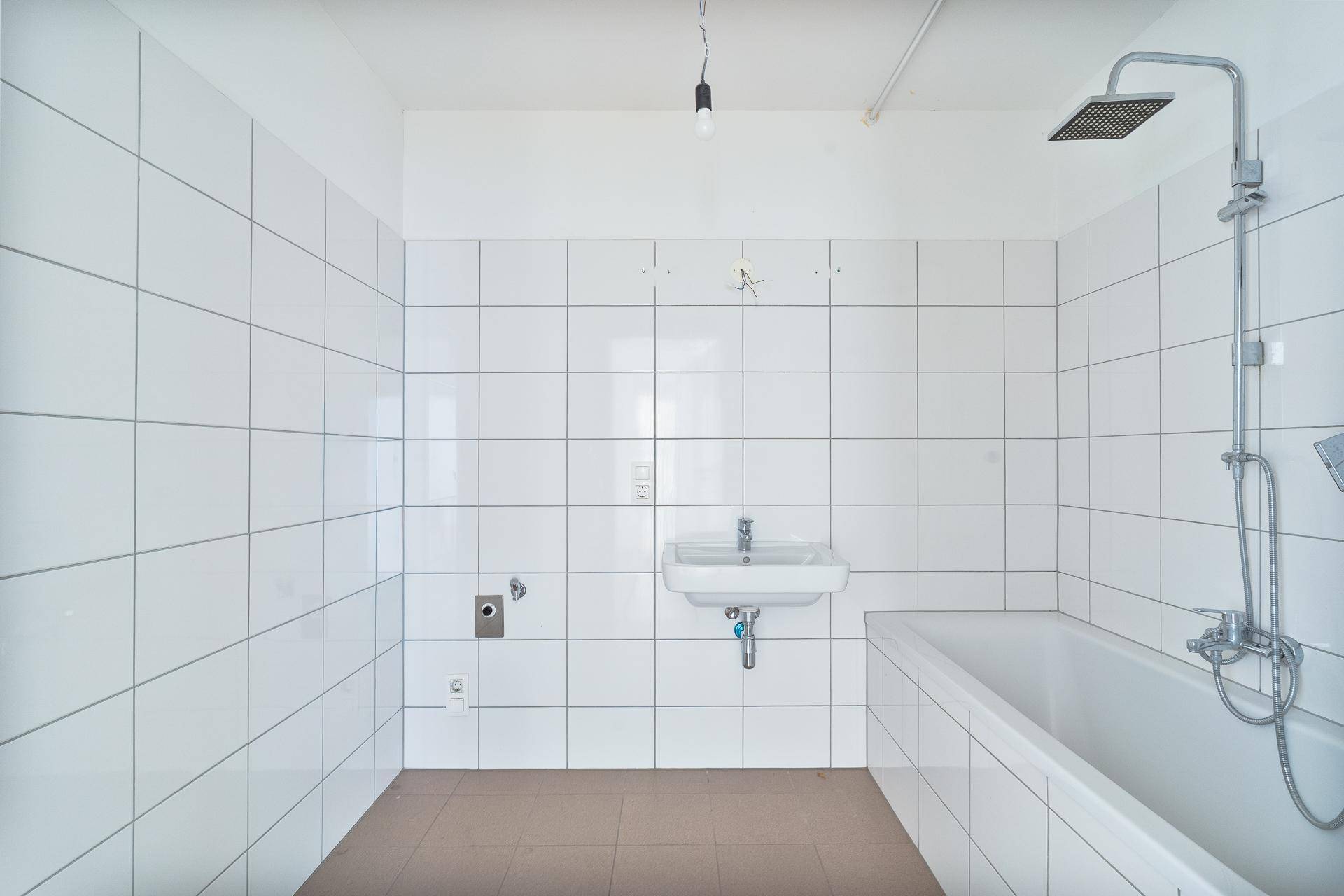 Weiß gefliestes Badezimmer mit Badewanne und Duschvorrichtung, funktional und sauber.