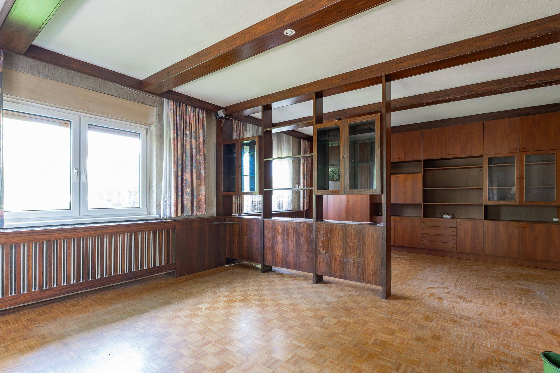 Geräumiges Wohnzimmer mit Holzbalken, Parkettboden und Einbauschränken.