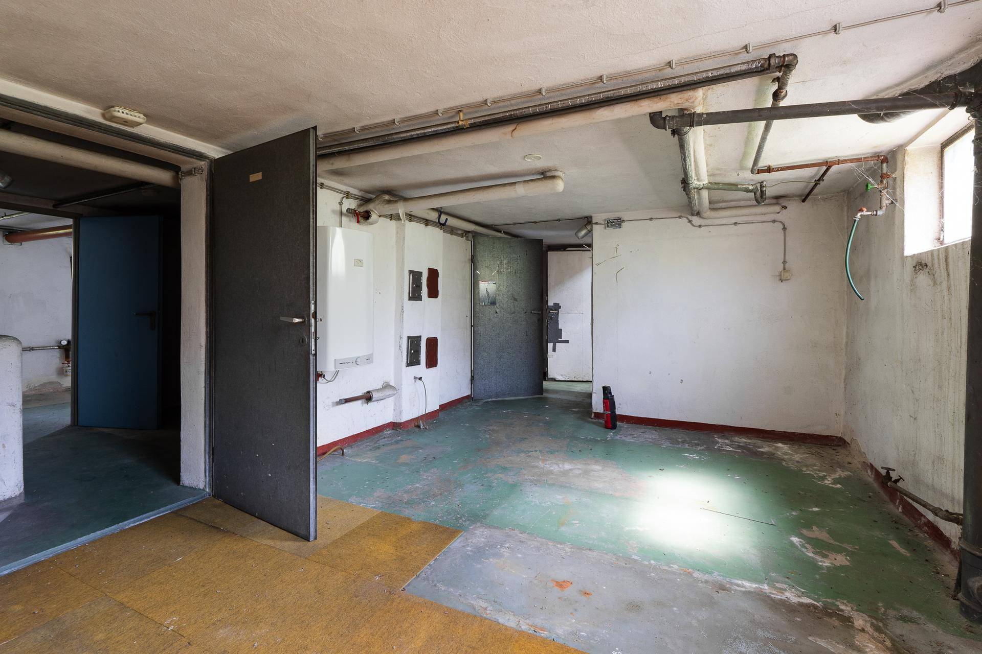 Geräumiger Kellerraum mit mehreren Türen und sichtbaren Leitungen.