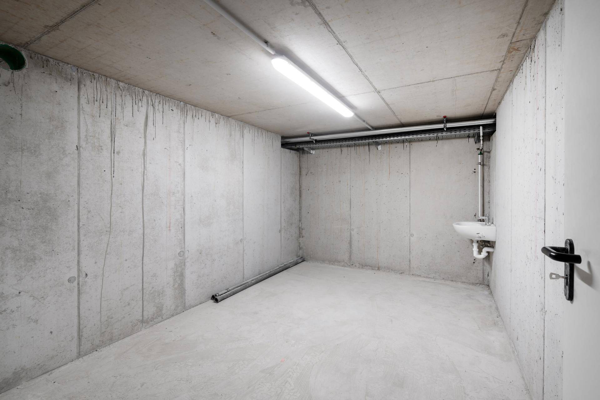 Funktionaler Kellerraum mit Betonwänden, Waschbecken und sichtbaren Installationen.