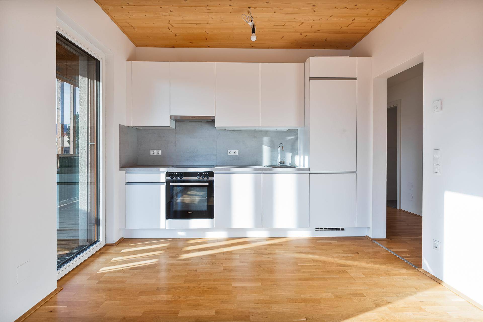Moderne Einbauküche mit weißen Schränken, integriertem Backofen und Holzboden.