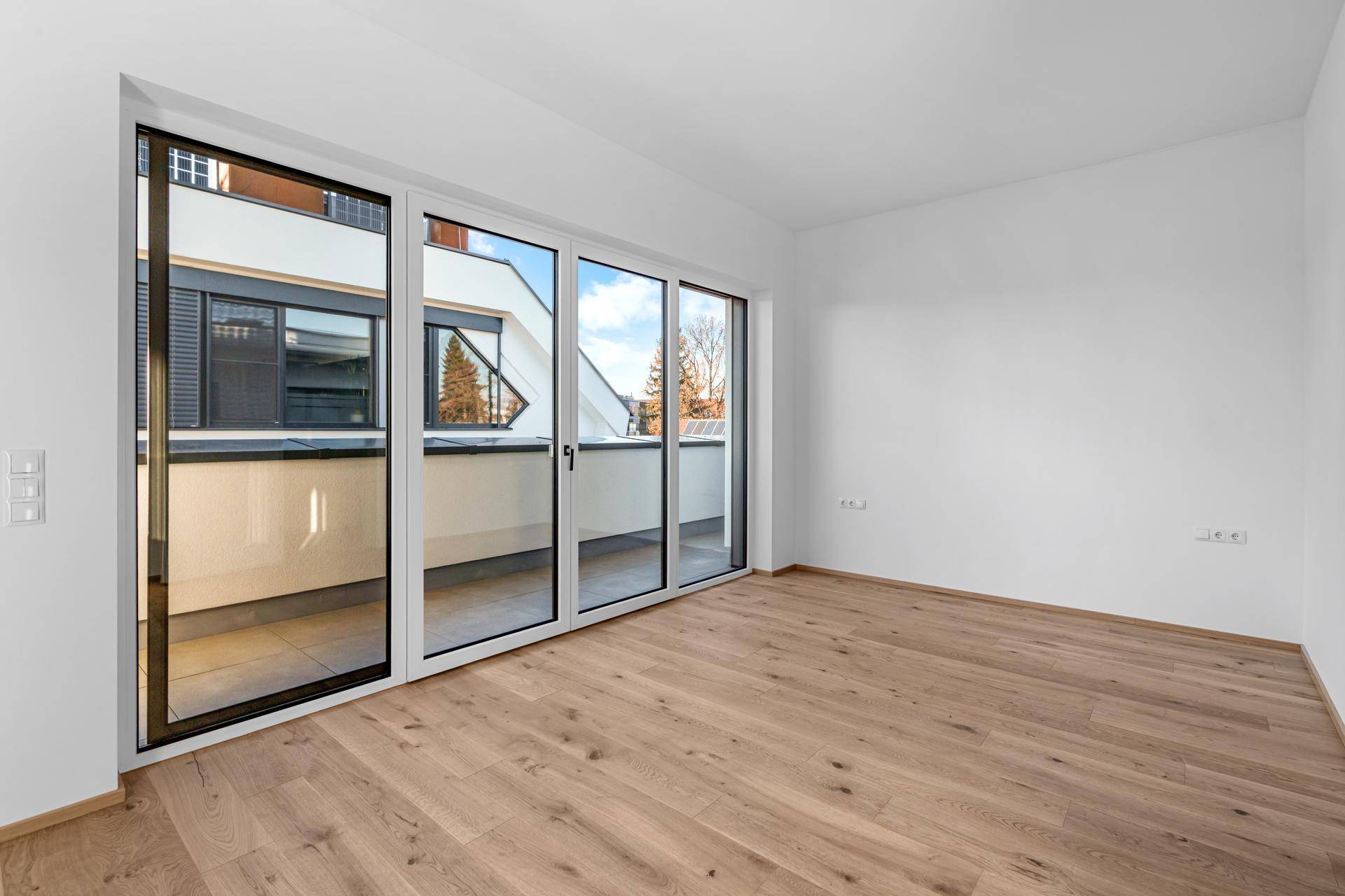 Helles Schlafzimmer mit Holzparkett und großen Fenstern, die Zugang zu einem Balkon bieten.