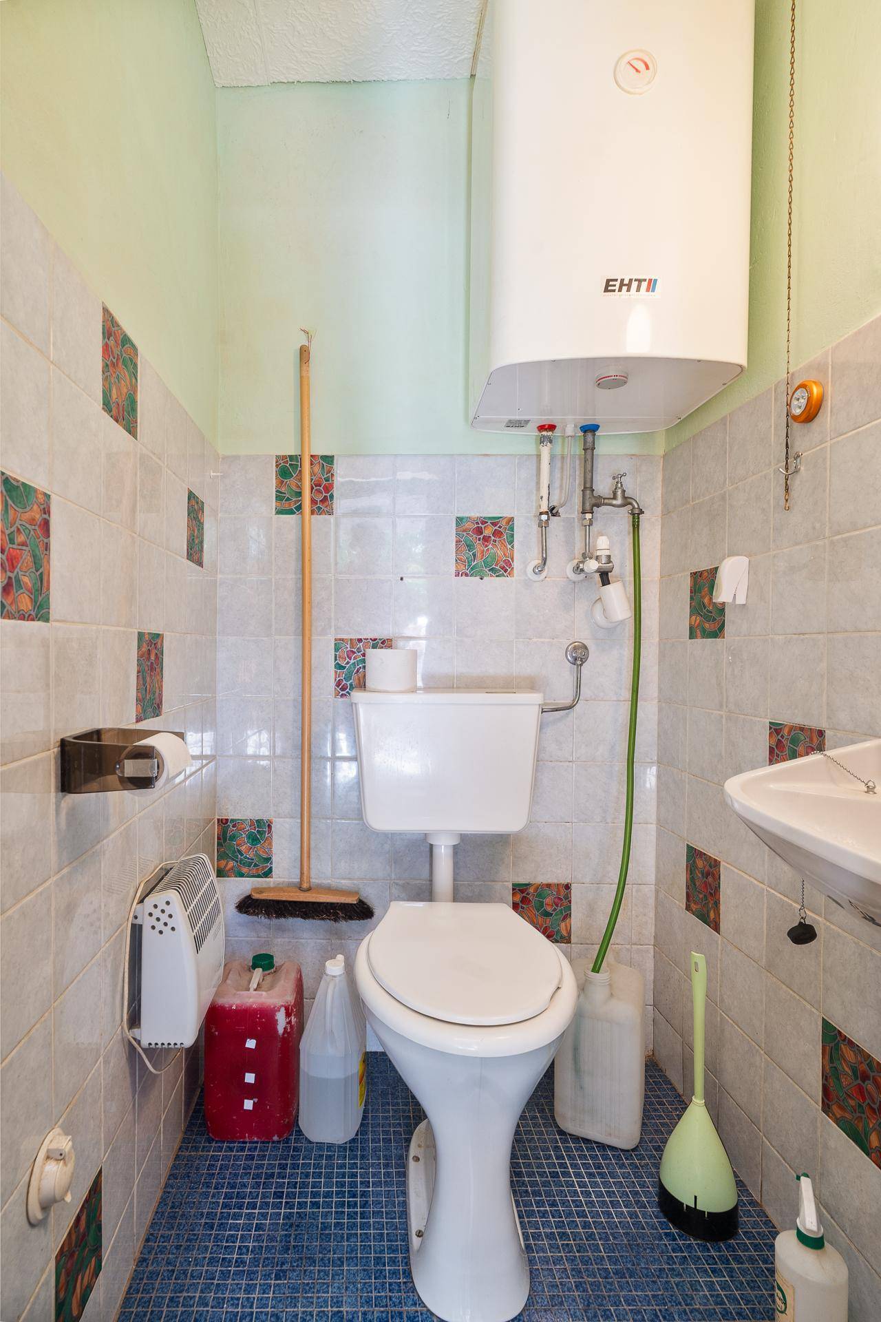 Separate Toilette mit Fliesen im 80er-Jahre-Stil und einem Warmwasserboiler an der Wand.