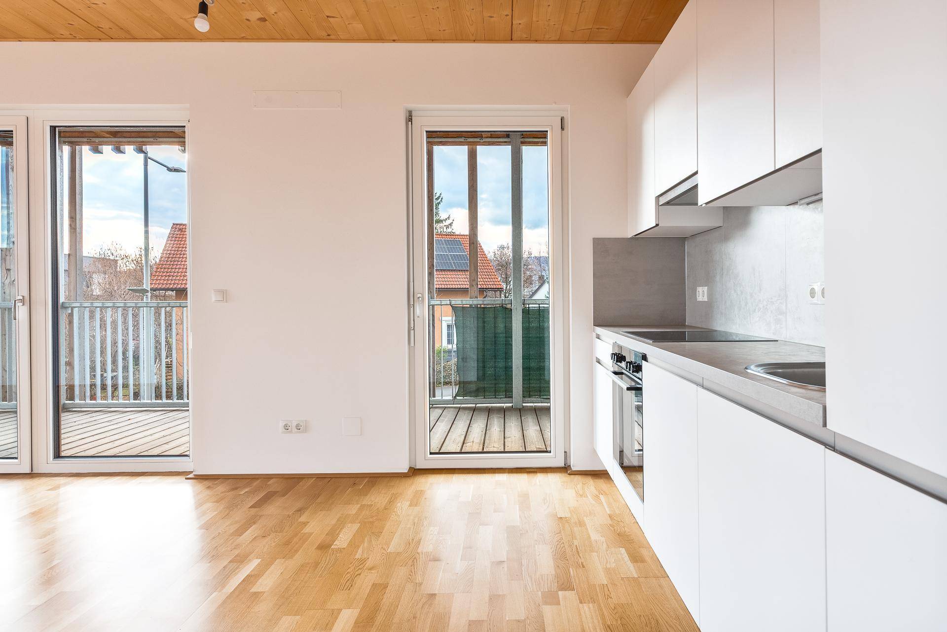 Helle Küche mit weißen Schränken, Holzboden und Zugang zu einem Balkon.