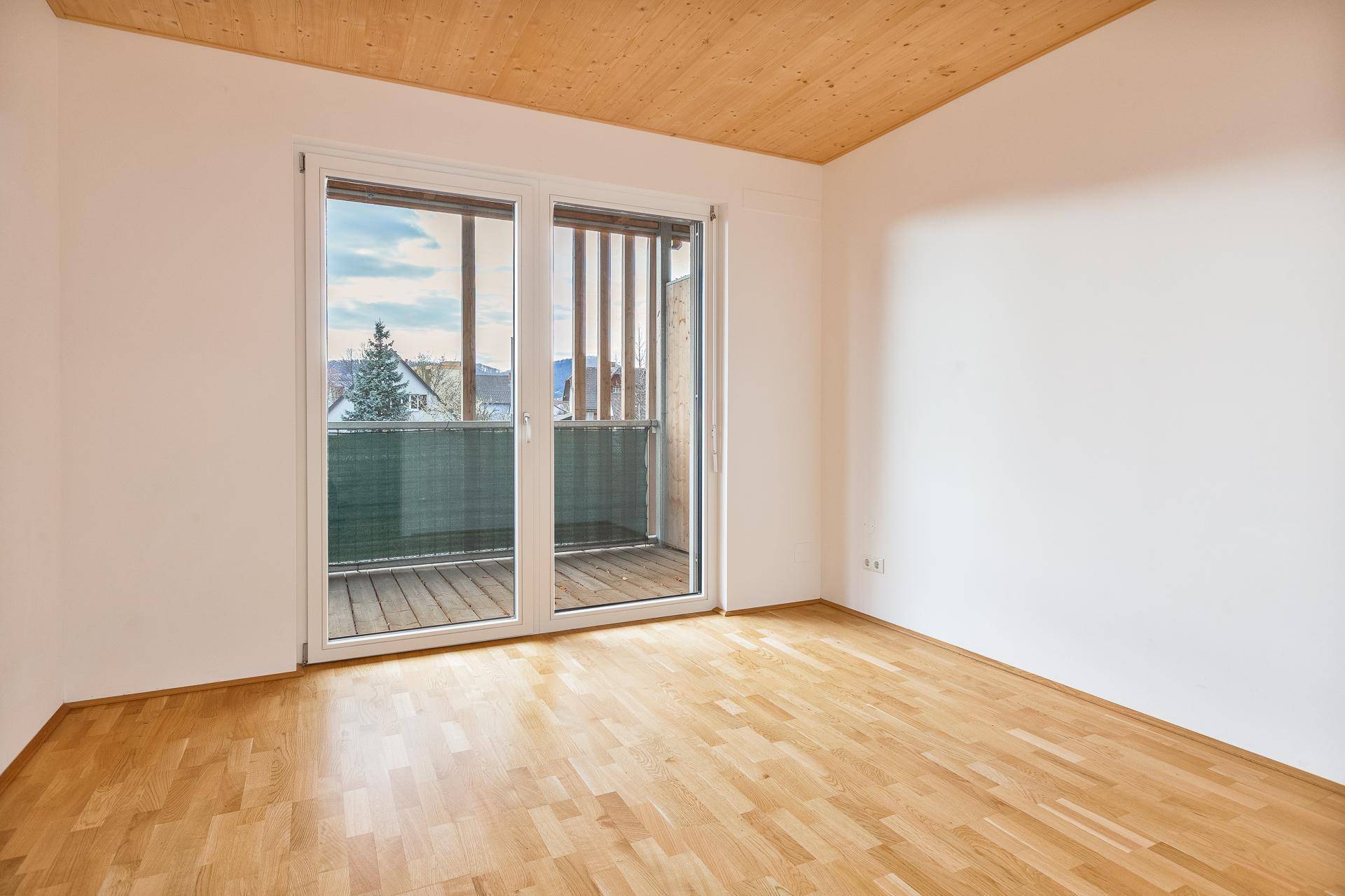 Geräumiges Zimmer mit Holzboden, Holzdecke und großen Fenstern zum Balkon.