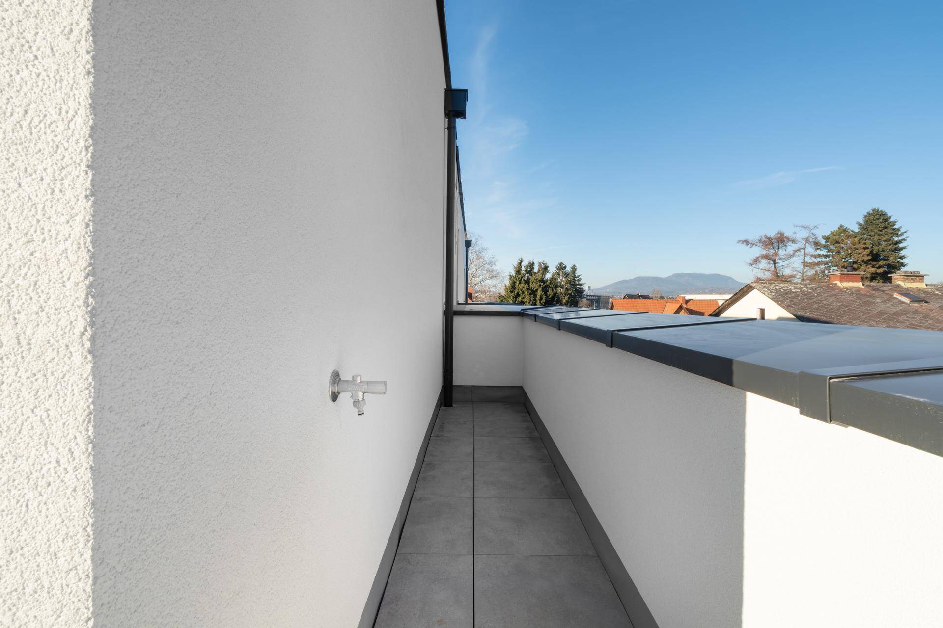 Kleiner, schmaler Balkon mit Wasseranschluss und Blick auf die Dächer der Umgebung.