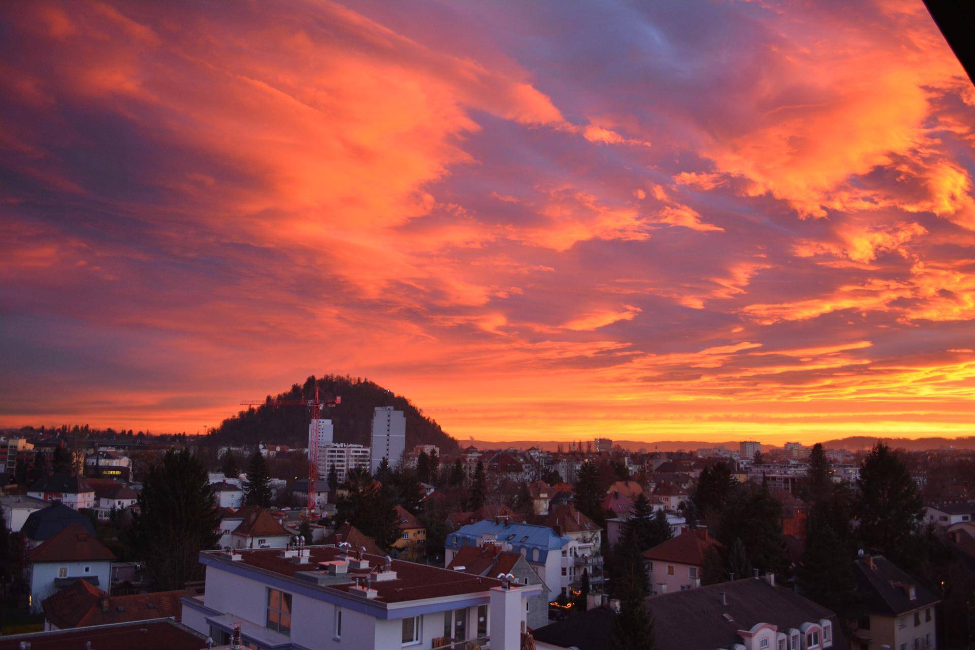 Spektakulärer Sonnenuntergang über der Stadt mit leuchtend rotem Himmel und einem bewaldeten Hügel.
