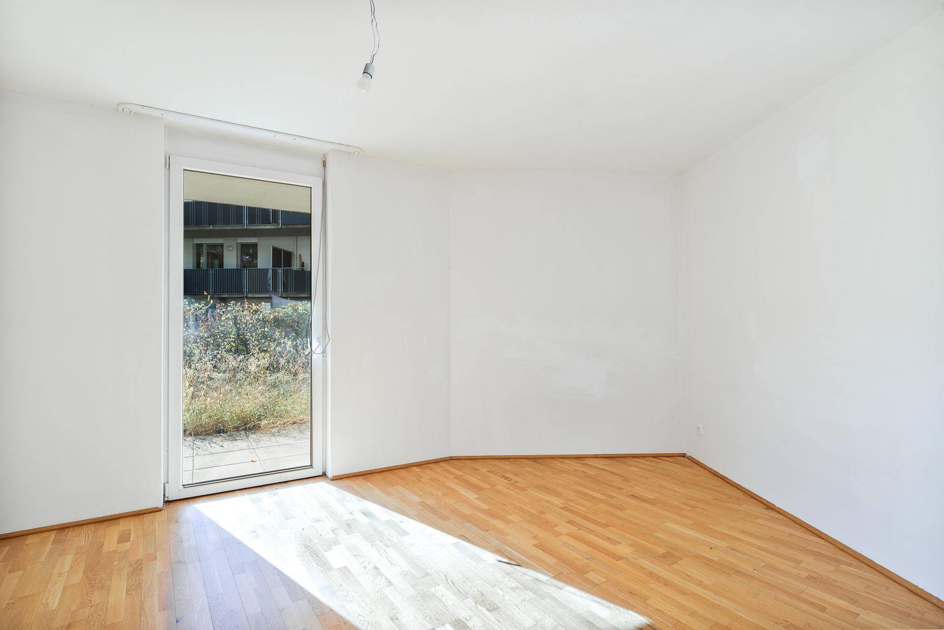 Heller Wohnraum mit Parkettboden und großer Glastür, die viel Tageslicht hereinlässt.