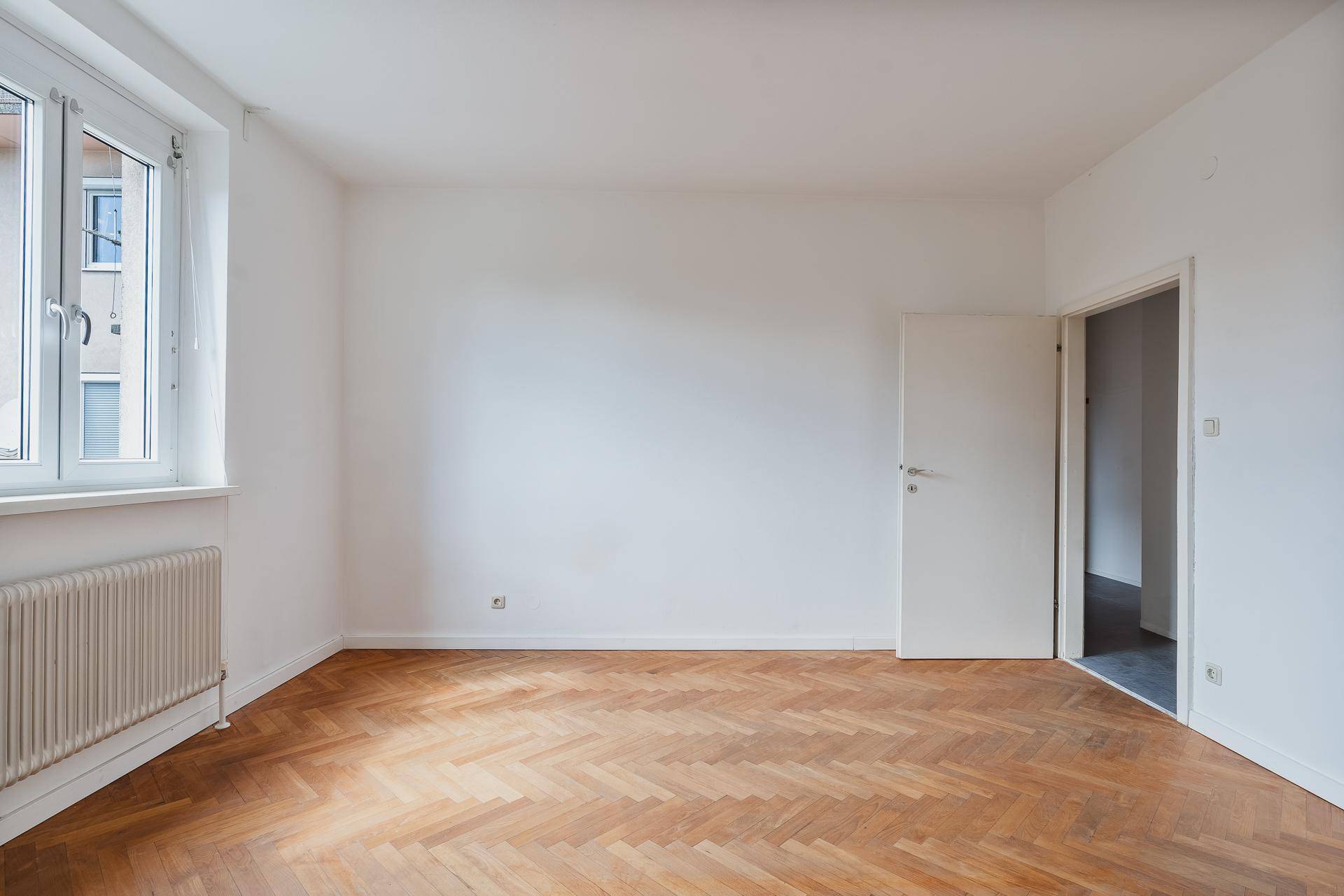 Leeres Zimmer mit Fischgrätparkettboden und Fenster, bereit zur individuellen Gestaltung.