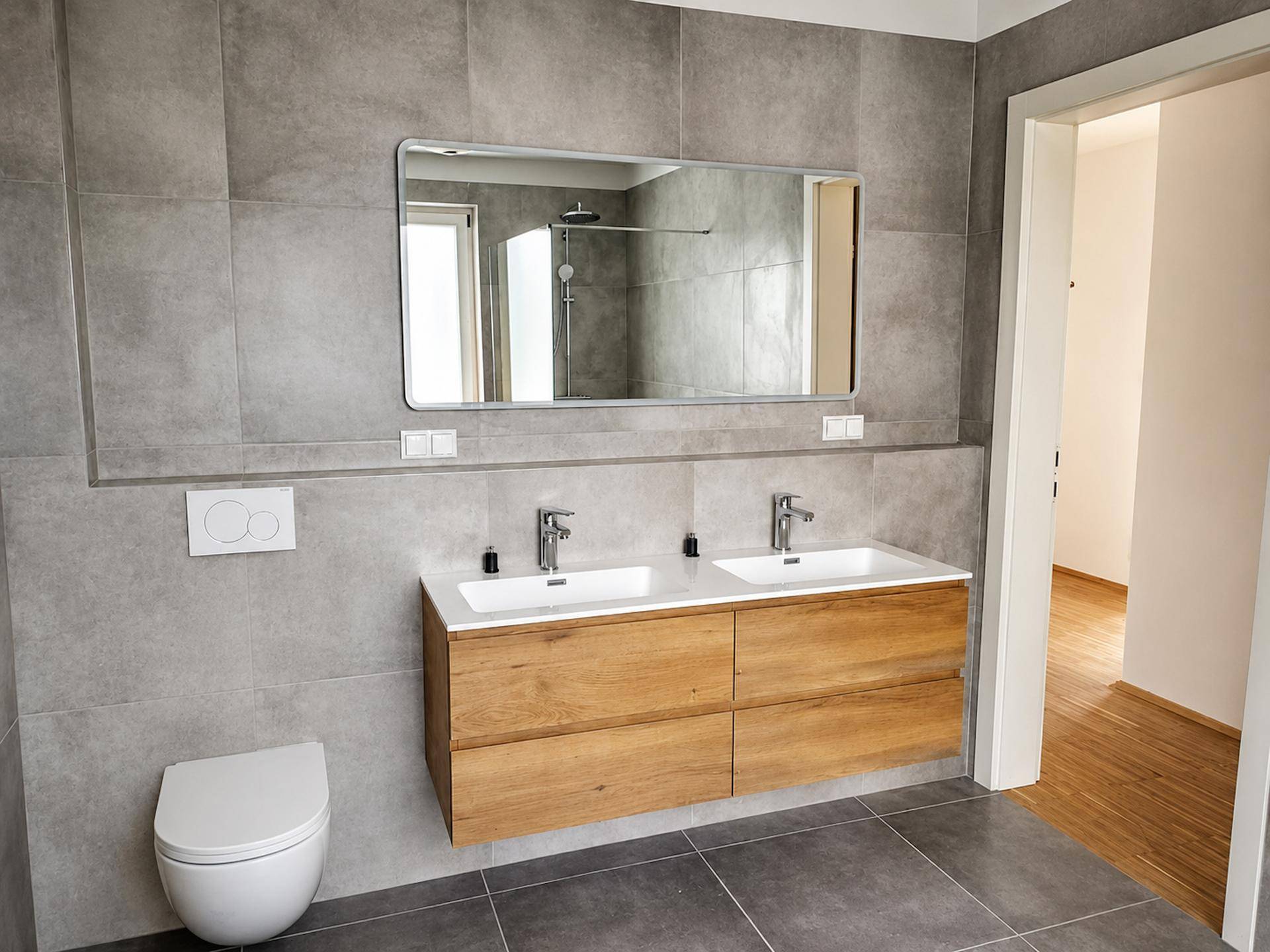 Modernes Badezimmer mit Doppelwaschbecken, schwebendem Holzunterschrank und grauen Fliesen.