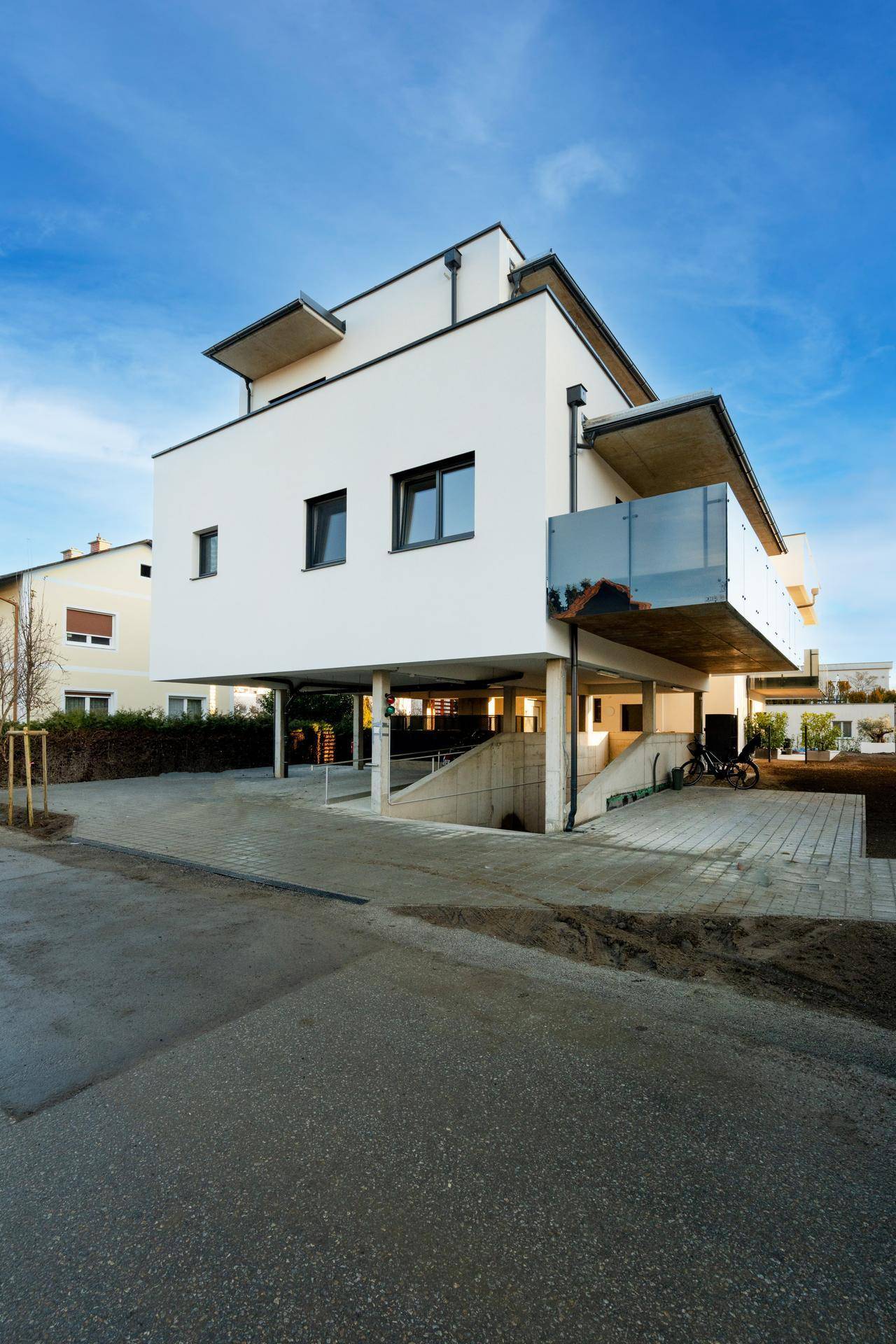 Modernes Wohnhaus mit markanter Architektur, Balkonen und unterirdischer Parkzufahrt.
