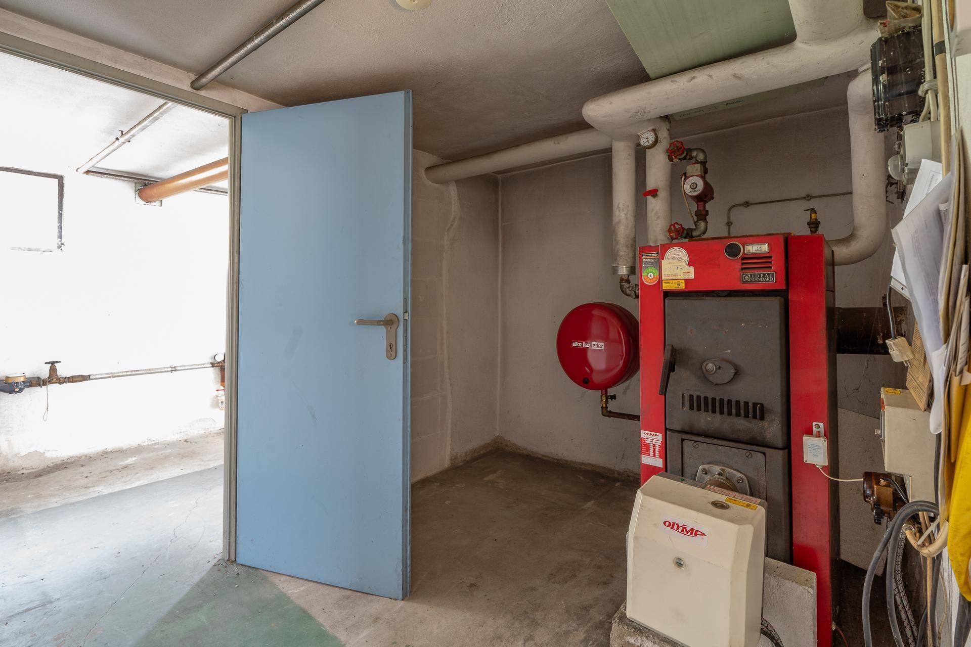 Heizungsraum im Keller mit großem Heizkessel und blauer Tür.