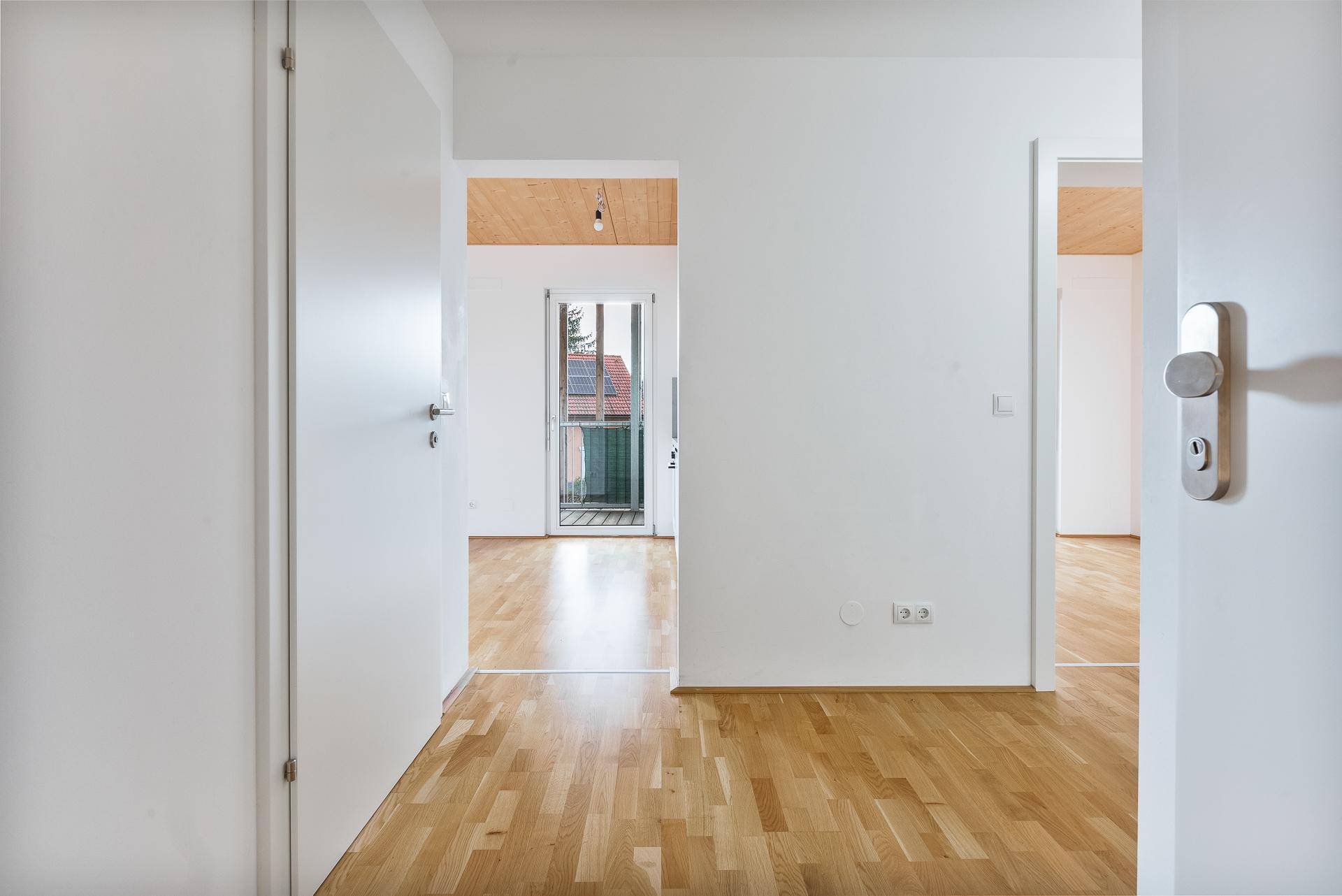 Heller Flur mit Holzboden und weißen Wänden, der zu verschiedenen Räumen führt.