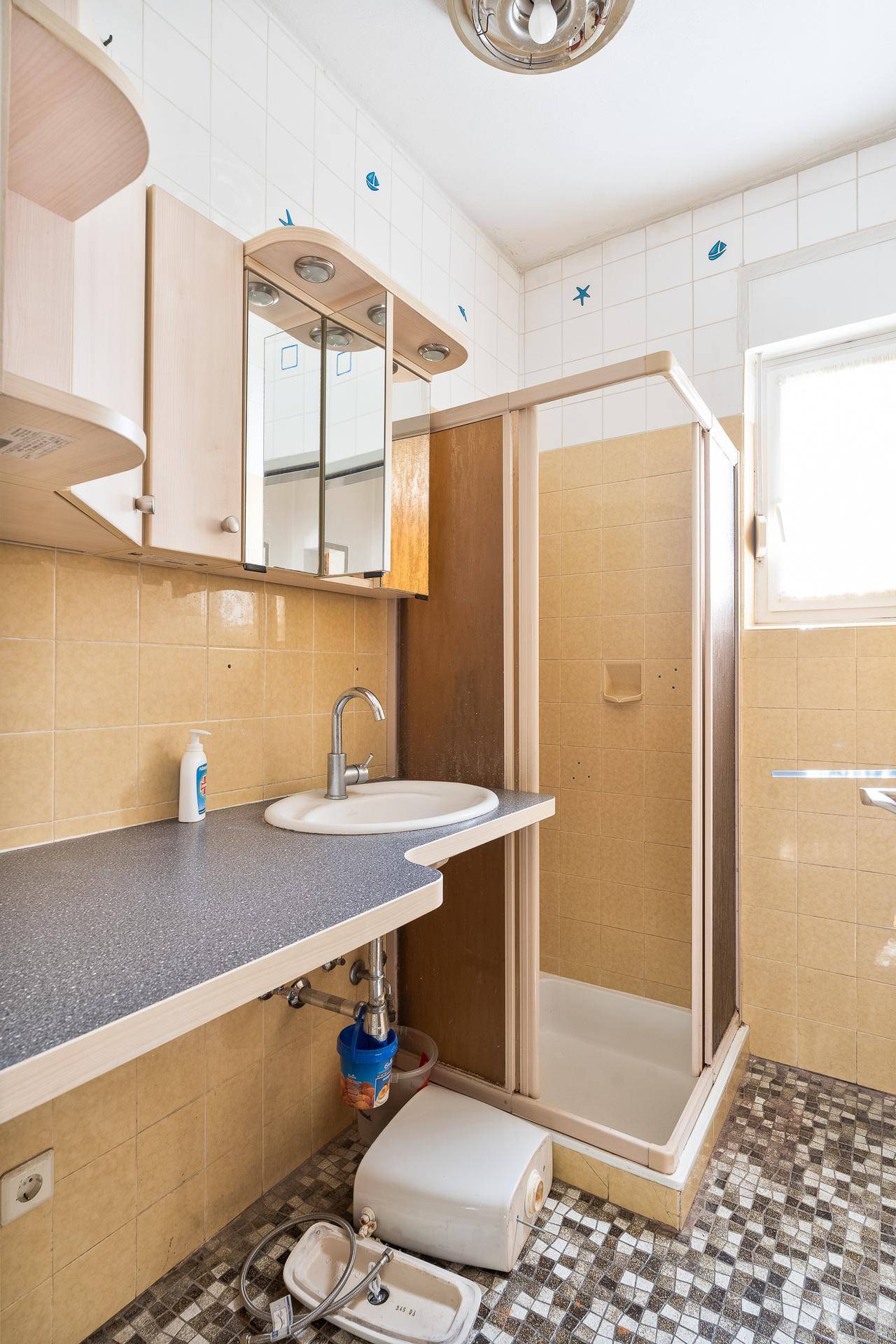 Badezimmer mit Duschkabine, Einzelwaschbecken und gemusterten Bodenfliesen.