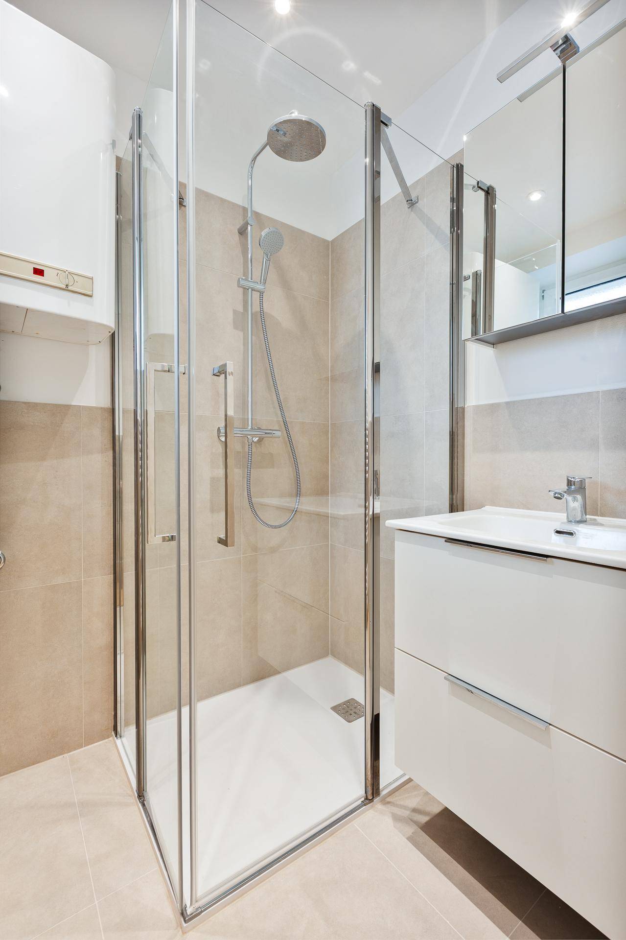 Modernes Badezimmer mit Glasduschkabine, Einzelwaschbecken und beigefarbenen Fliesen.