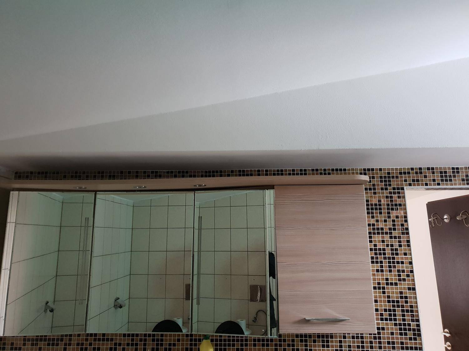 Badezimmerspiegelkabinett über einem Waschbecken mit Mosaikfliesenwand und Holzdetails.