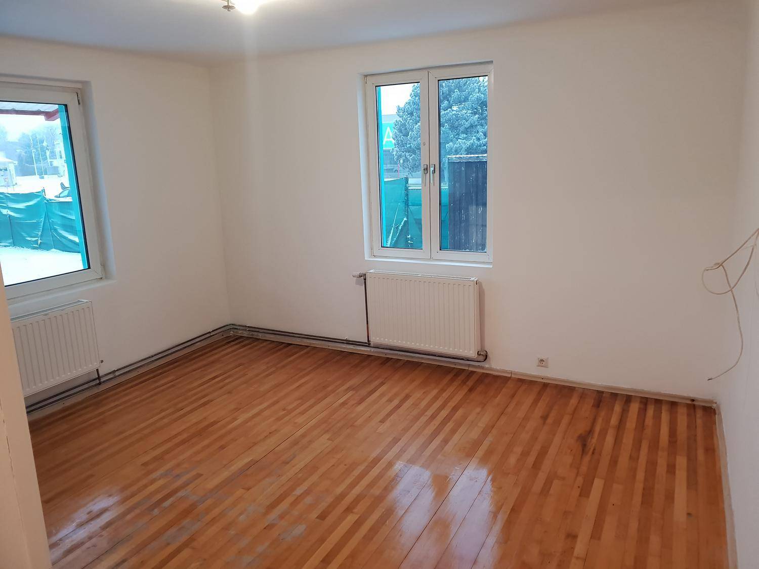 Geräumiger, heller Raum mit Holzboden, zwei Fenstern und Heizkörpern, ideal für Schlafzimmer.