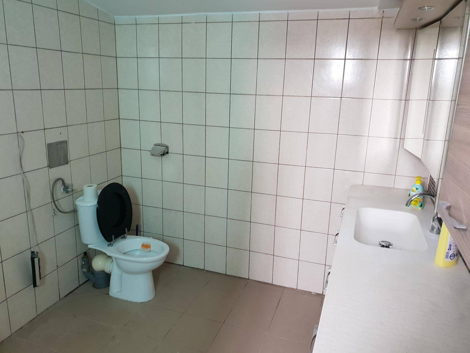 Badezimmer mit WC, Waschbecken und hellen Fliesen an Wänden und Boden.