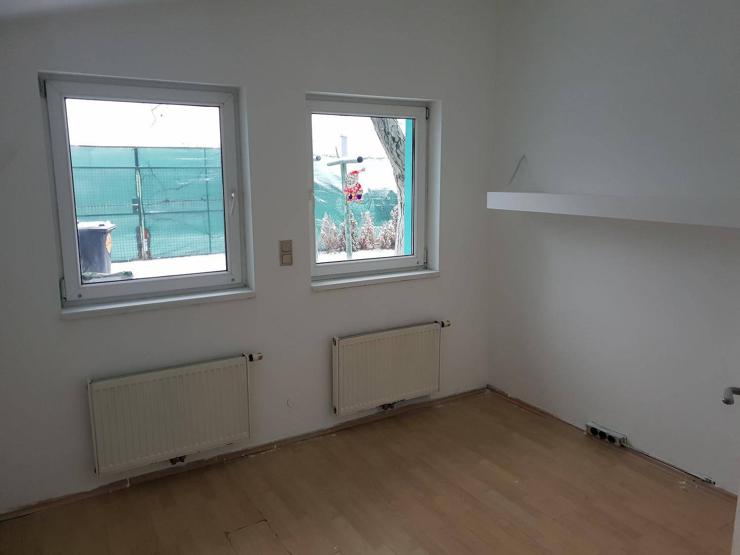 Heller Raum mit Holzboden, zwei Fenstern und Heizkörpern, bietet viel natürliches Licht.