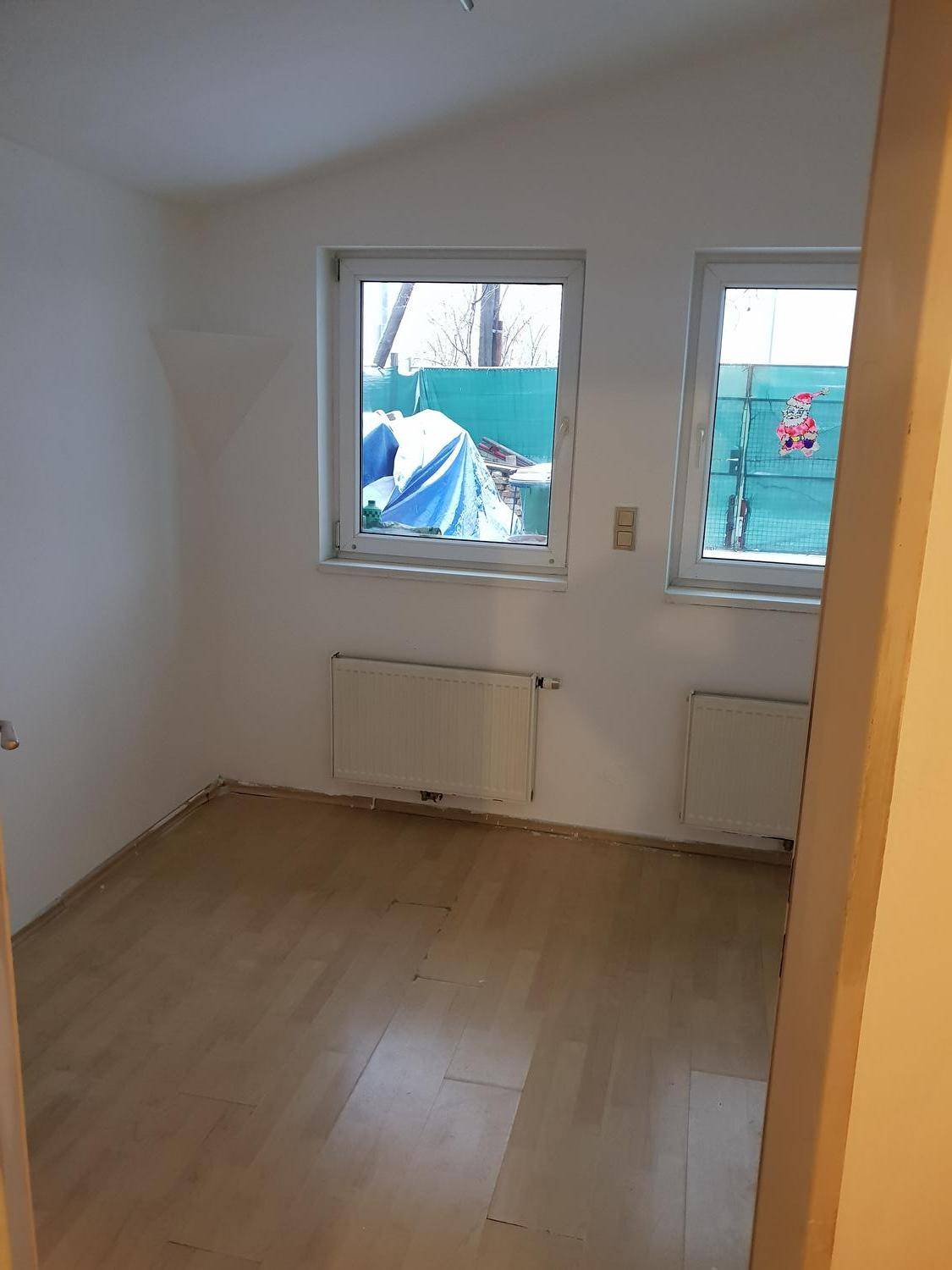 Kleinerer Raum mit Holzboden, zwei Fenstern und Heizkörpern, geeignet als Kinder- oder Arbeitszimmer.