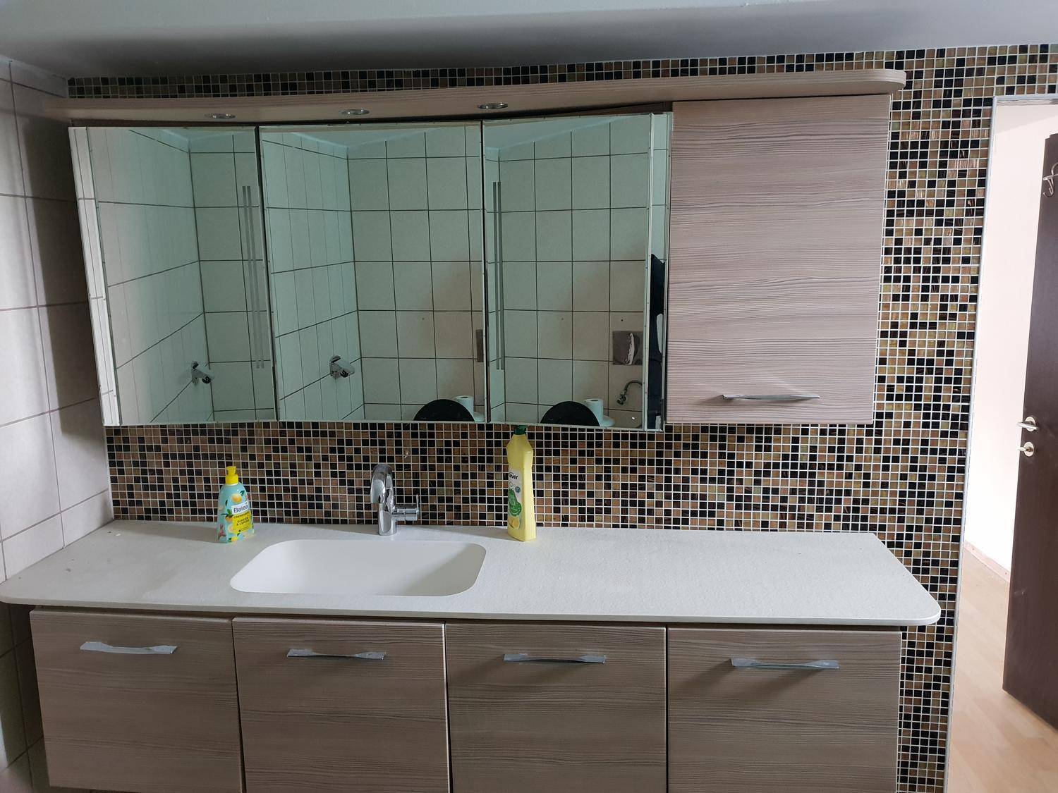 Badezimmer mit modernem Waschtisch, Einzelwaschbecken und Spiegelkabinett über Mosaikfliesen.