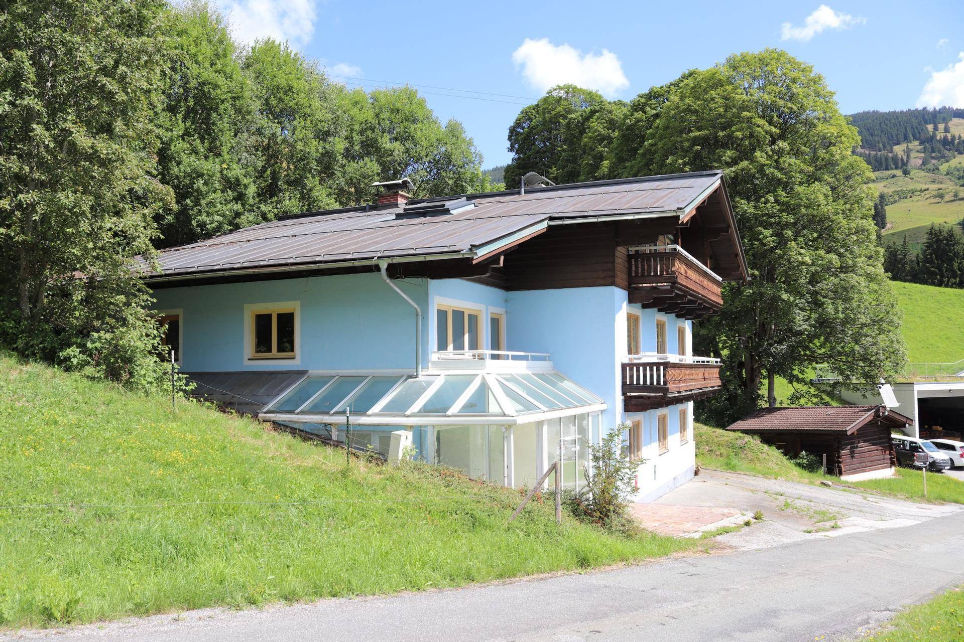 Seitenansicht des Hauses mit Wintergarten und Zufahrt, eingebettet in die grüne Landschaft.