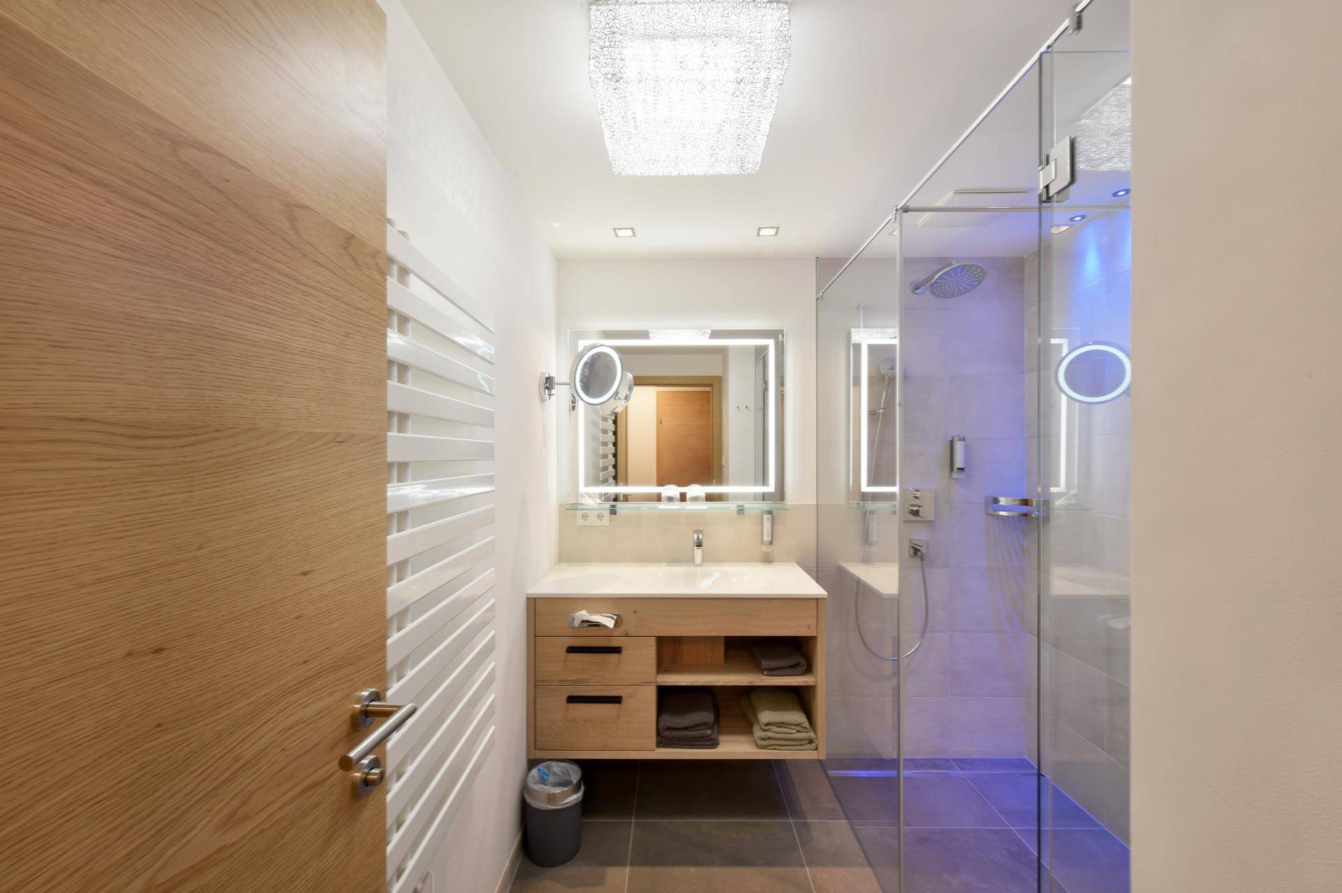 Elegantes Badezimmer mit begehbarer Dusche, Holzwaschtisch und beheiztem Handtuchhalter.