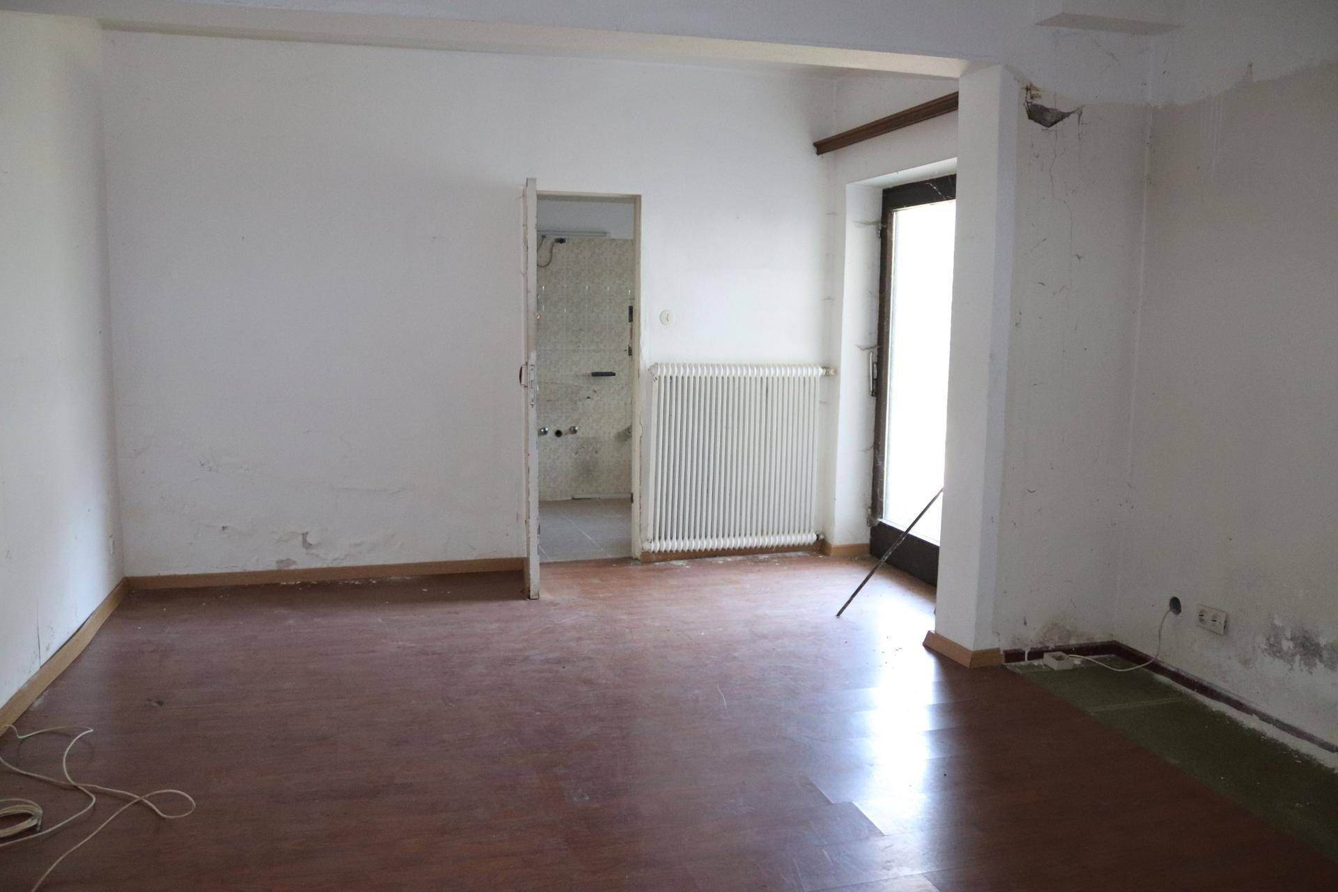 Unmöblierter Raum mit weißen Wänden, dunklem Boden und einem Heizkörper, der auf Renovierung wartet.