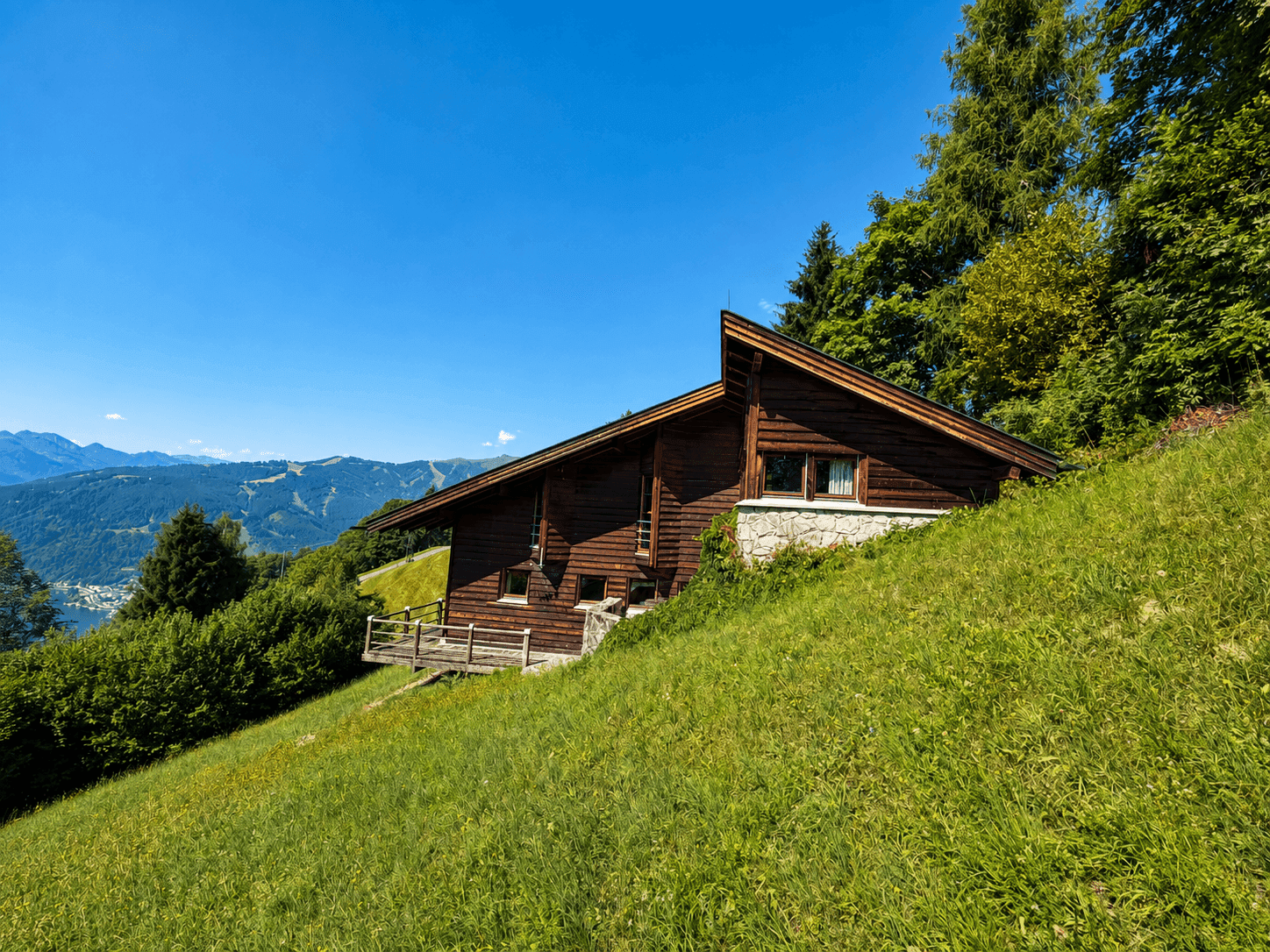 Holzhaus in Hanglage mit Blick auf die umliegende Berglandschaft und grüne Wiesen.