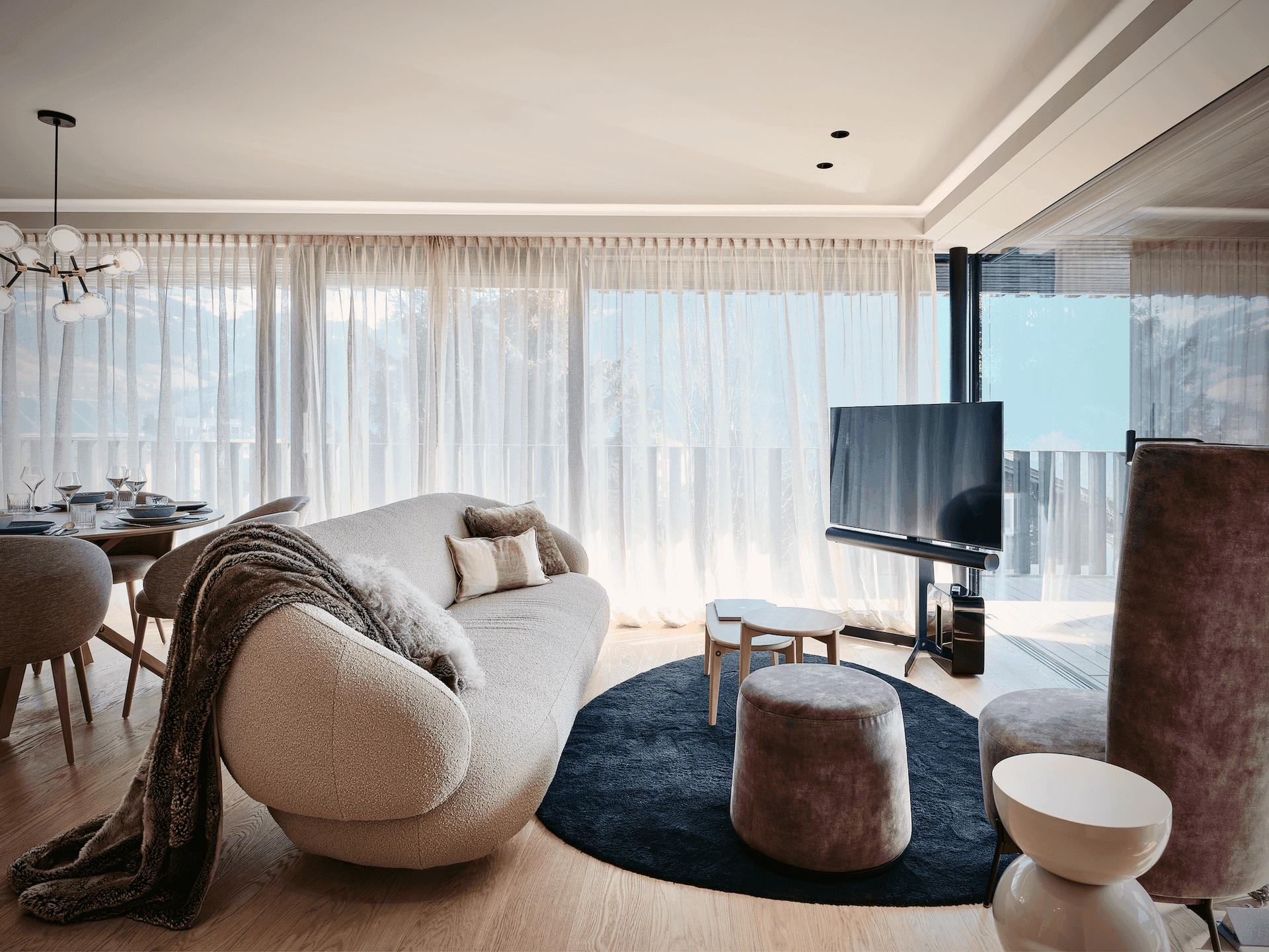Elegantes Wohnzimmer mit geschwungenem Sofa, modernem Kronleuchter und großen Fenstern mit Vorhängen.