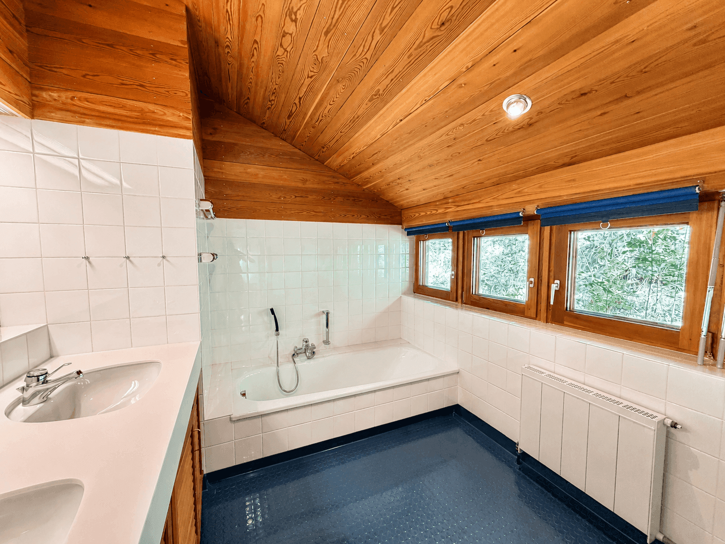 Helles Badezimmer mit Badewanne, weißen Fliesen und Holzdachschräge.