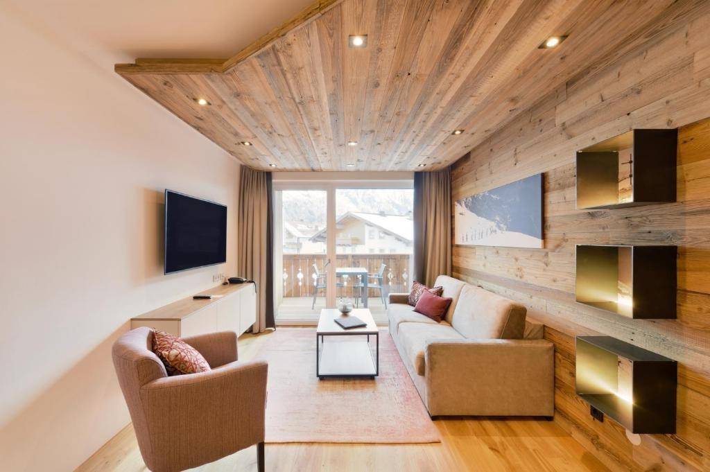 Gemütliches Wohnzimmer mit Holzwänden, Sofa und Zugang zu einem möblierten Balkon.
