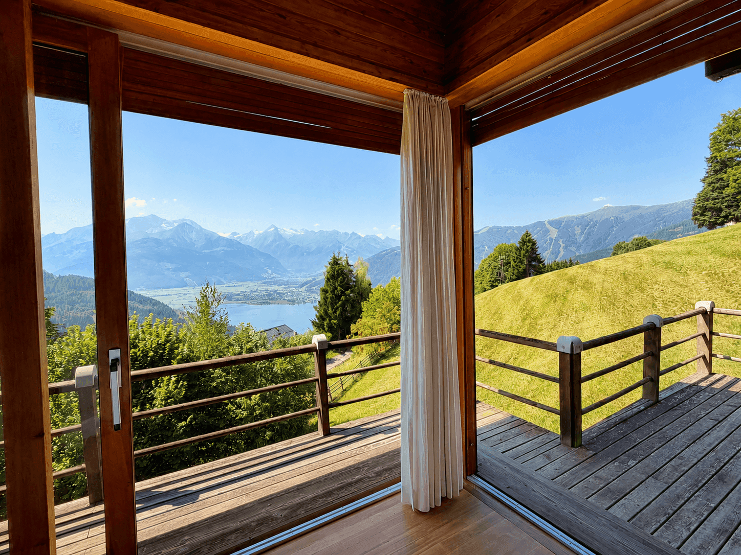 Atemberaubender Blick auf den See und die Berge von einer Holzterrasse mit großen Fenstern.