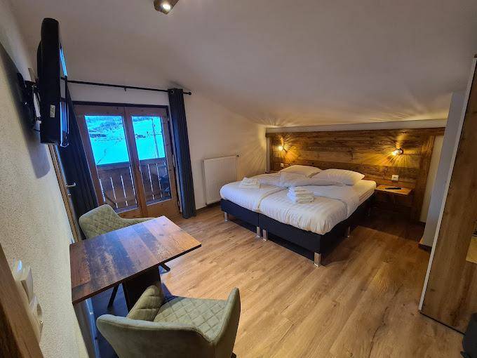 Gemütliches Schlafzimmer mit Holzboden, Doppelbett und Zugang zu einem kleinen Balkon.
