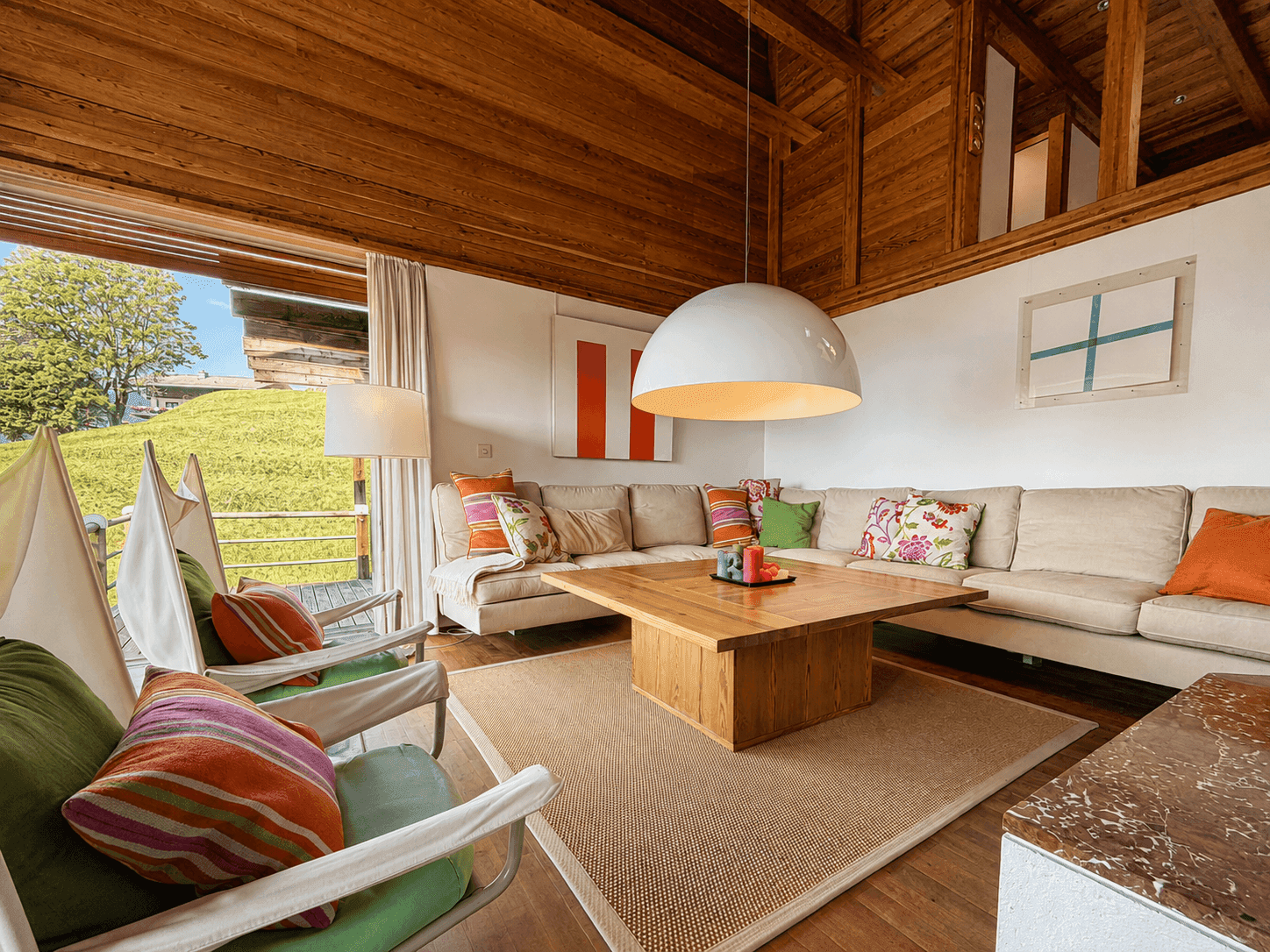 Gemütliches Wohnzimmer im Chalet-Stil mit Holzbalkendecke, bequemen Sofas und Zugang zur Terrasse.