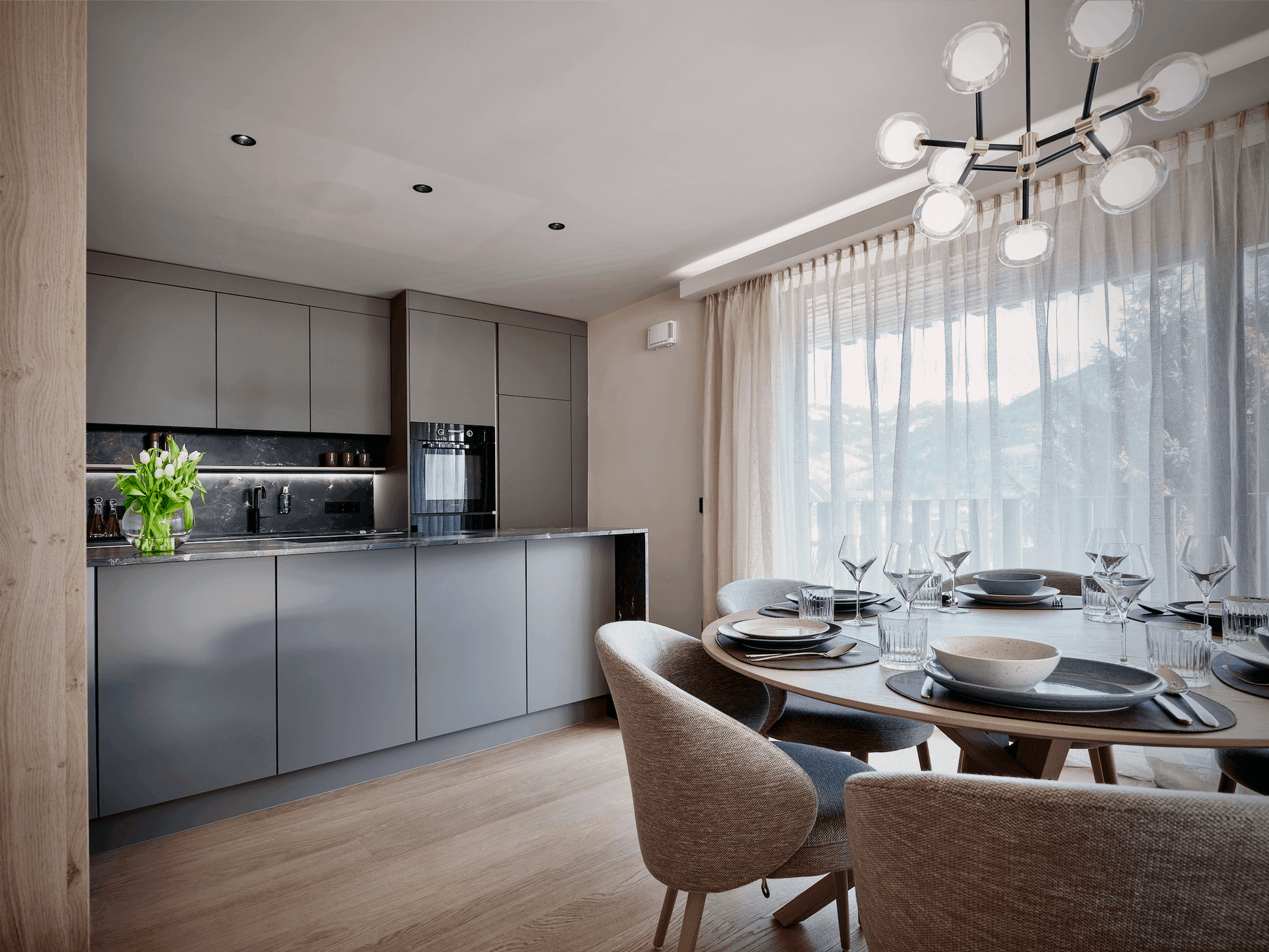 Moderne Küche mit grauen, grifflosen Schränken und Essbereich, elegant für Gäste gedeckt.