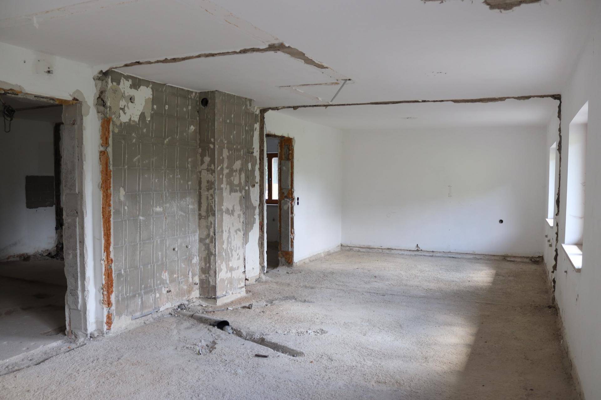 Innenraum im Rohbauzustand mit freigelegten Wänden und Boden, bereit für die Renovierung.