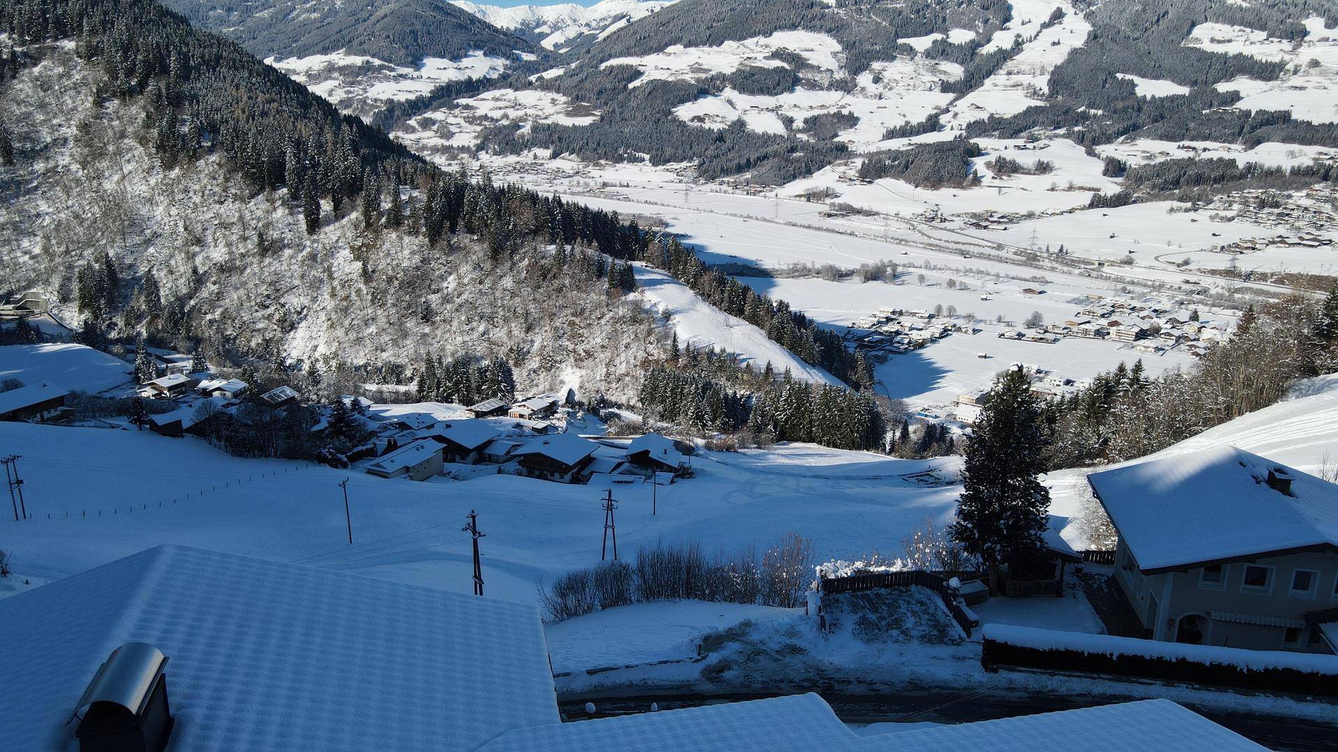 Weitläufiger Blick über das schneebedeckte Tal und die umliegenden Berge an einem sonnigen Tag.