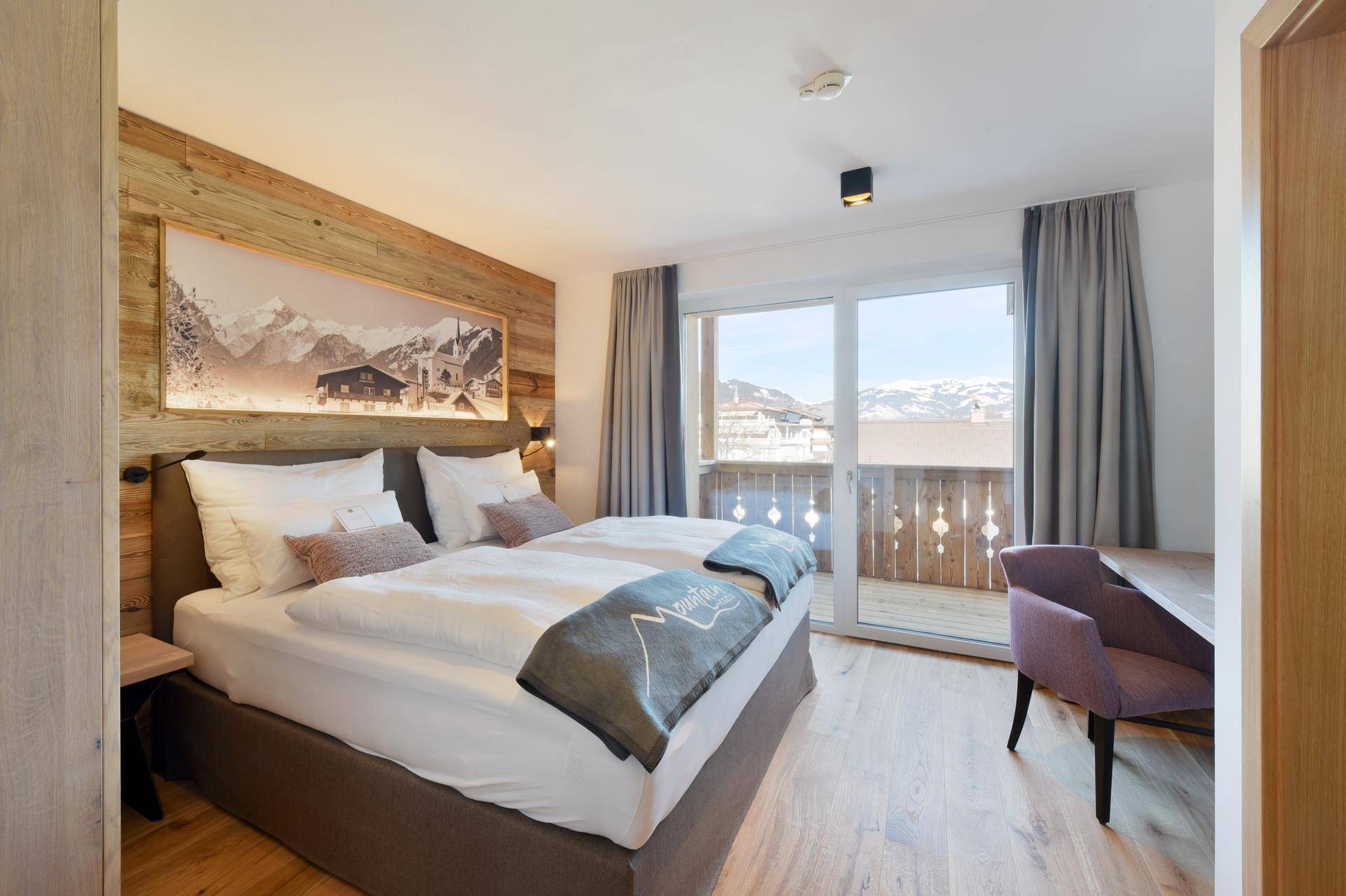 Helles Schlafzimmer mit Holzwand, Doppelbett und Bergblick vom Balkon.