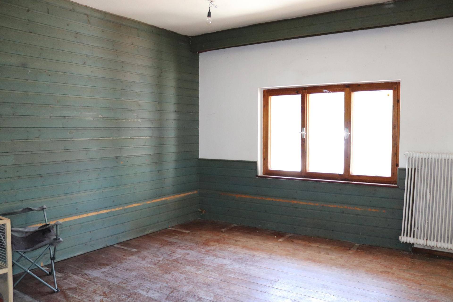 Unmöblierter Raum mit grüner Holzvertäfelung, Holzboden und einem Fenster.