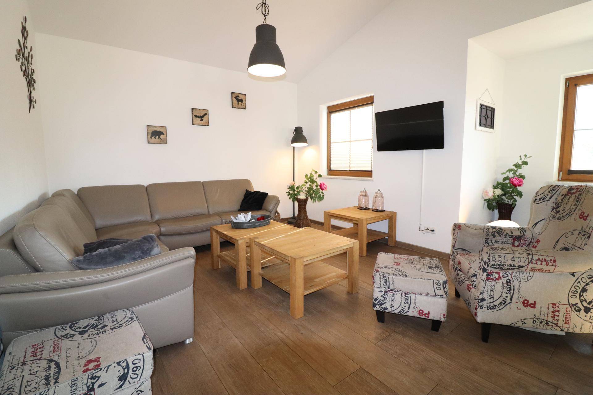 Helles Wohnzimmer mit beigem Ecksofa, Holztischen und Holzboden unter hohen Decken.