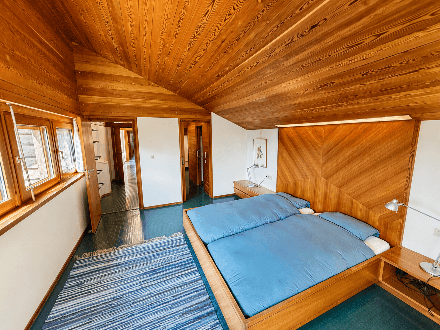 Gemütliches Schlafzimmer mit Holzdachschräge, Doppelbett und integrierten Holzmöbeln.