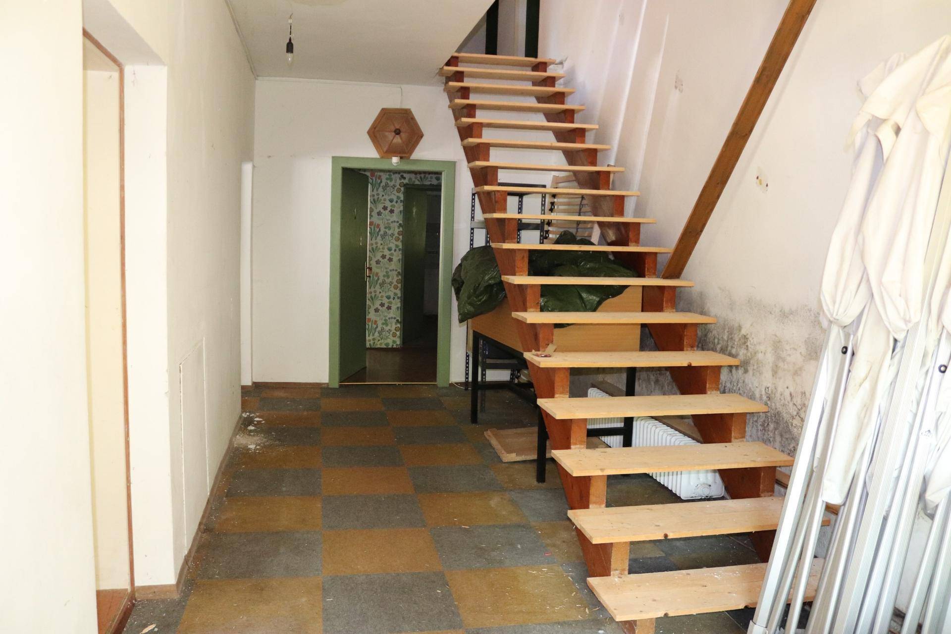 Flur mit Holztreppe, kariertem Fliesenboden und Zugang zu weiteren Räumen.