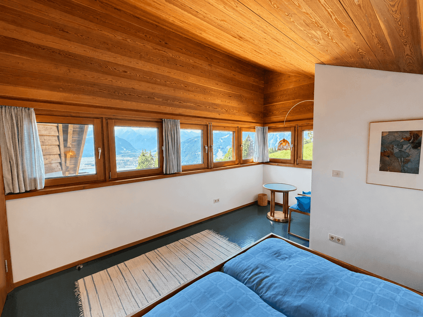 Helles Schlafzimmer mit mehreren Fenstern, Holzdachschräge und Bergblick.