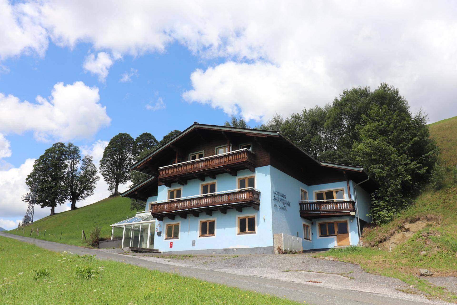 Das traditionelle Haus steht inmitten einer grünen Hügellandschaft unter einem blauen Himmel mit Wolken.